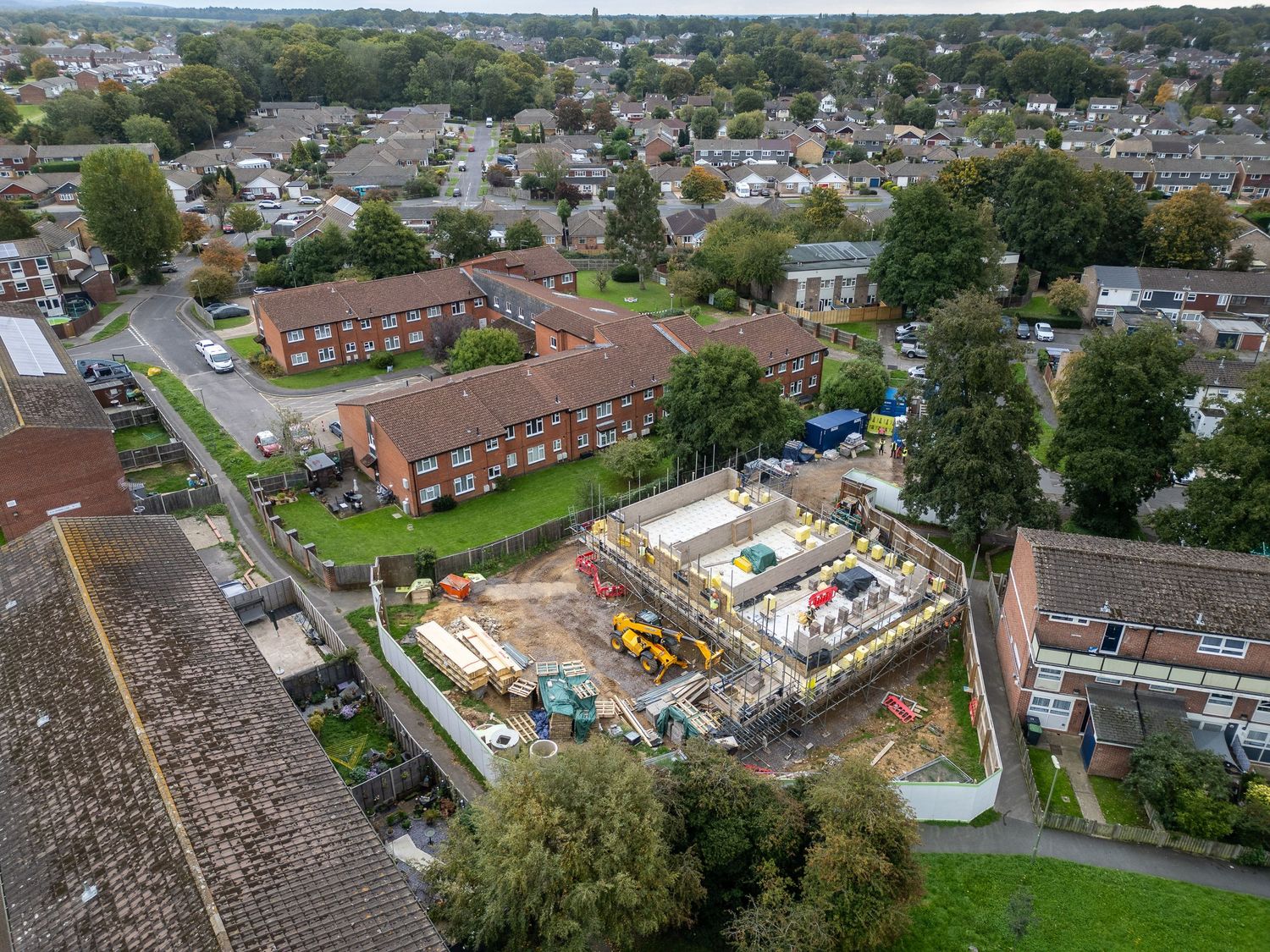 Aerial view of residential neighborhood with construction site and red brick buildings surrounded by trees.