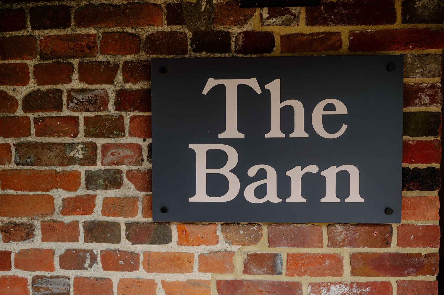 Weathered brick wall with vintage-style wooden signs spelling out 'The Barn' mounted on it.