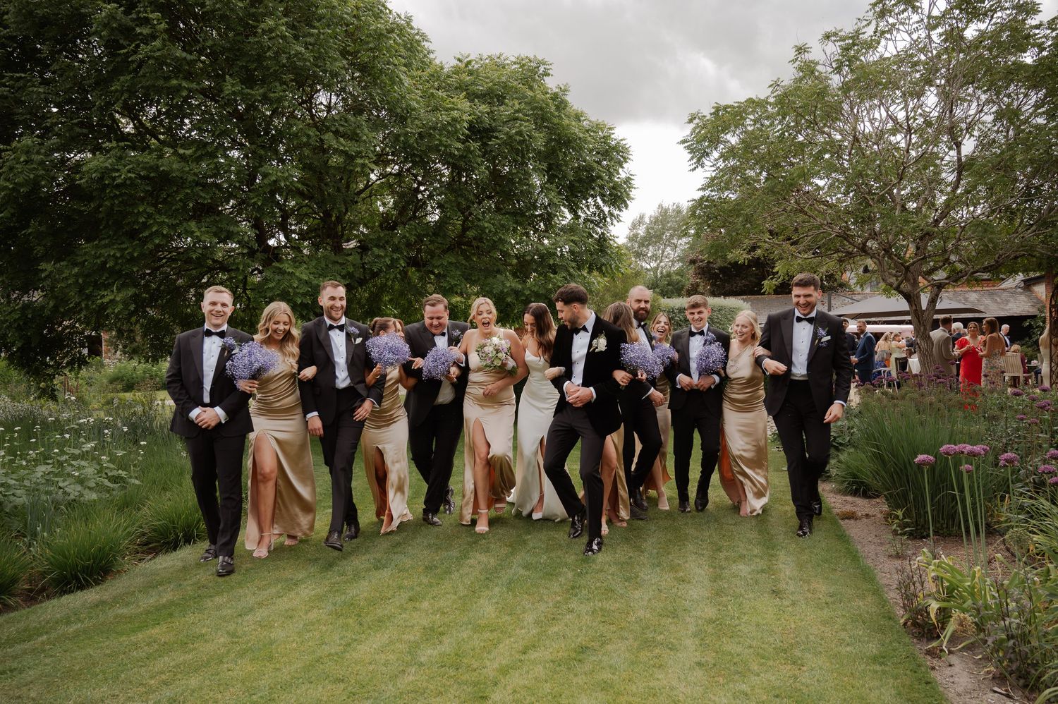 Wedding party members pose together on a lush green hillside during an outdoor celebration.