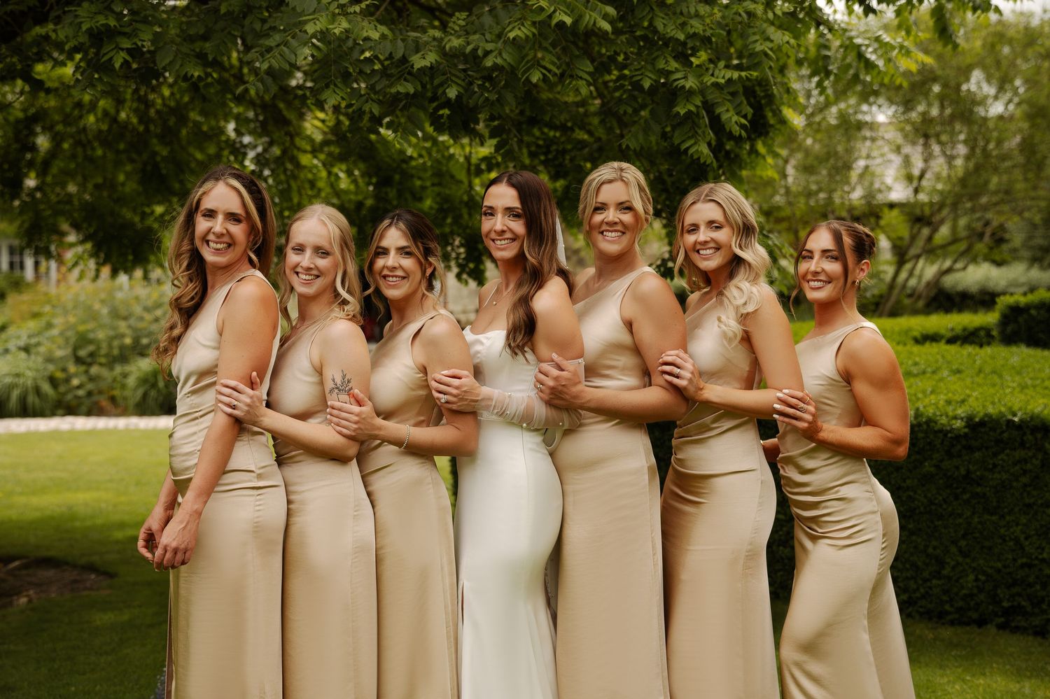 Bridesmaids wearing champagne-colored dresses pose together in a garden setting.