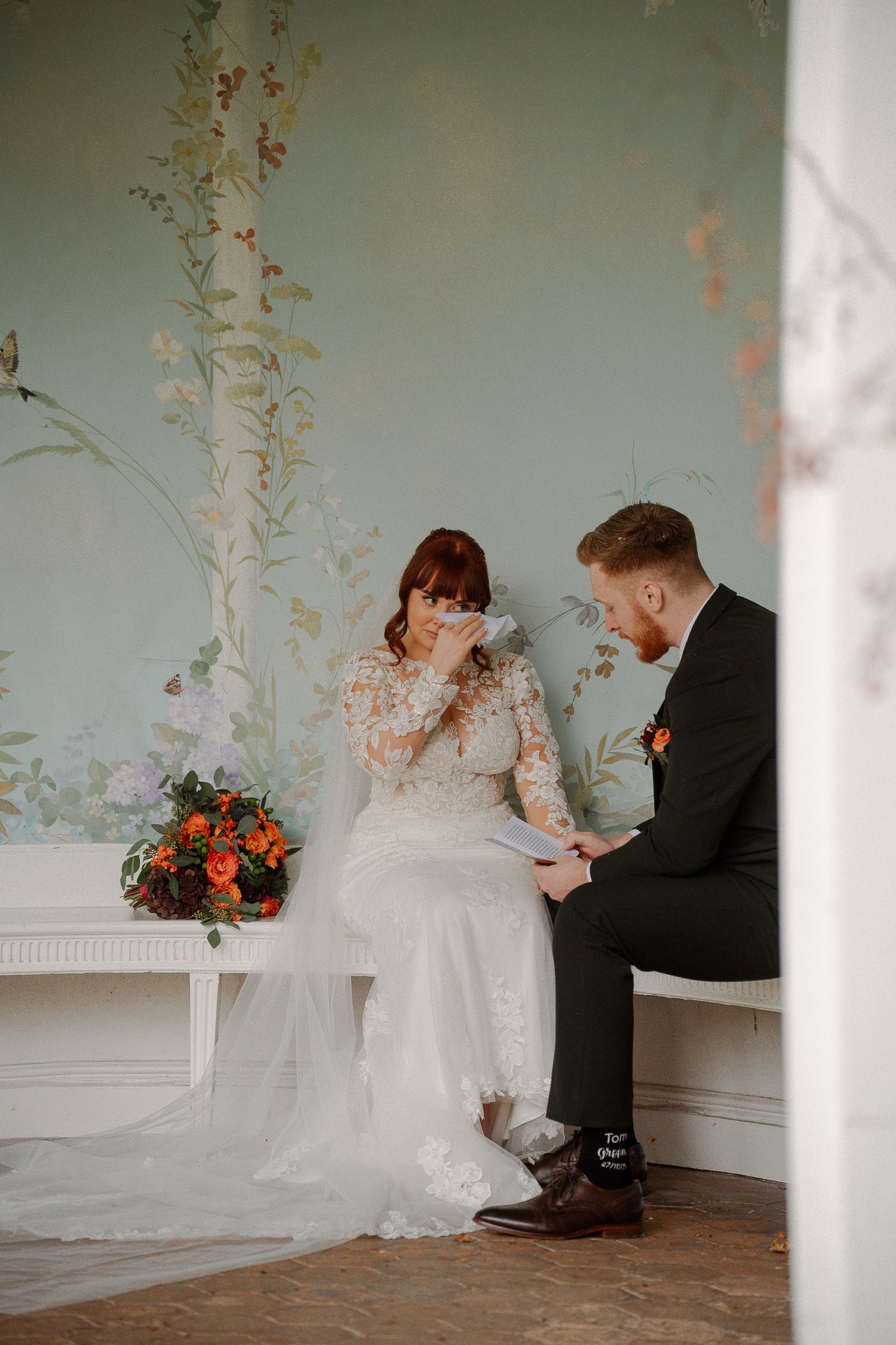 A couple shares a romantic moment in an elegant room with floral wallpaper during their wedding celebration.