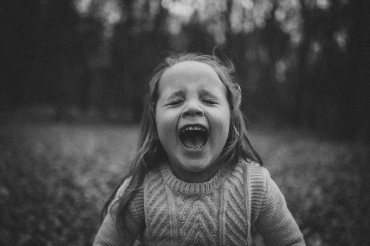 A joyful child wearing a knit sweater laughs while playing outdoors in a black and white photograph.