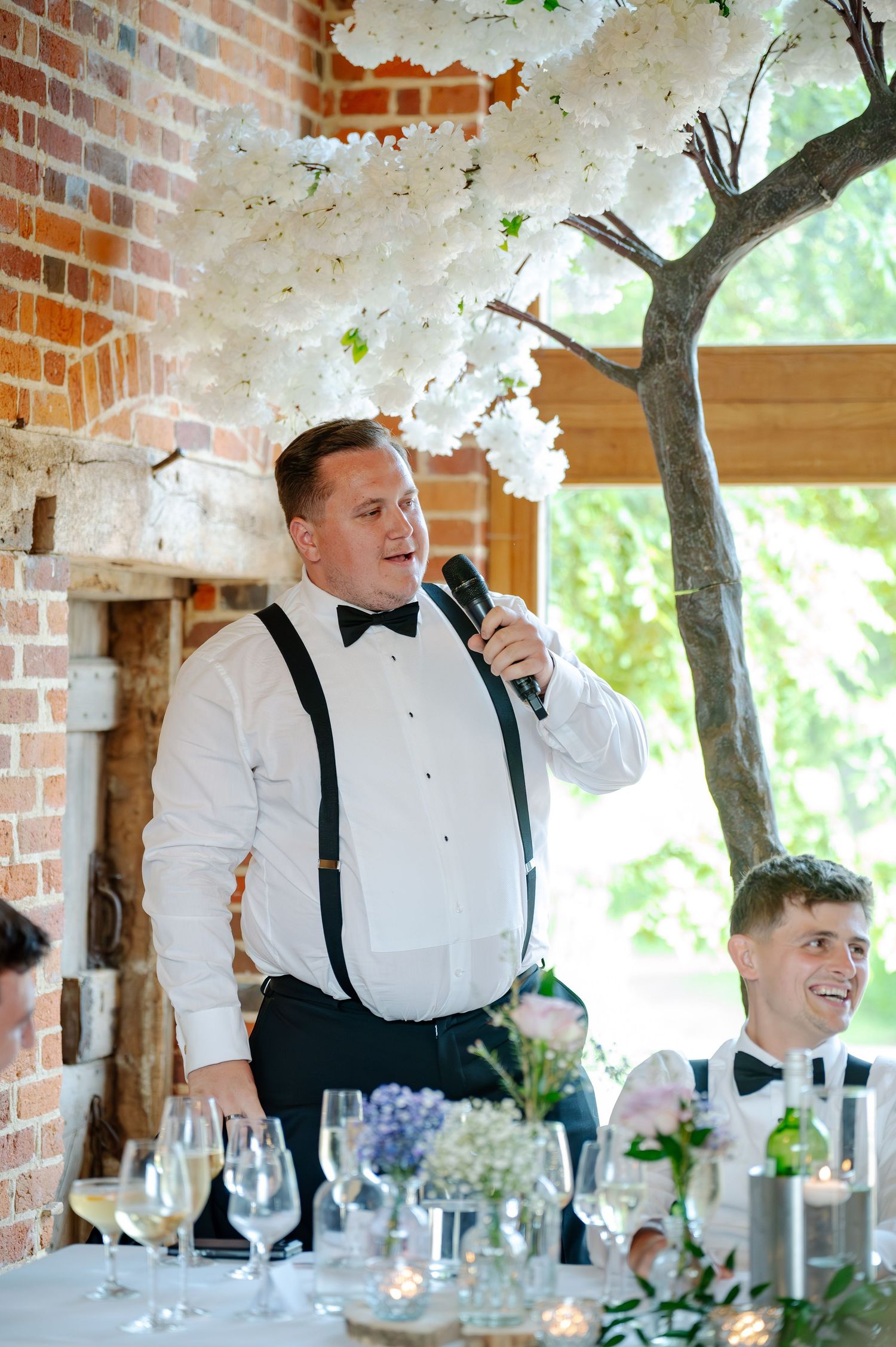 Groomsmen in white shirts and bow ties laughing together under decorative floral arrangements.