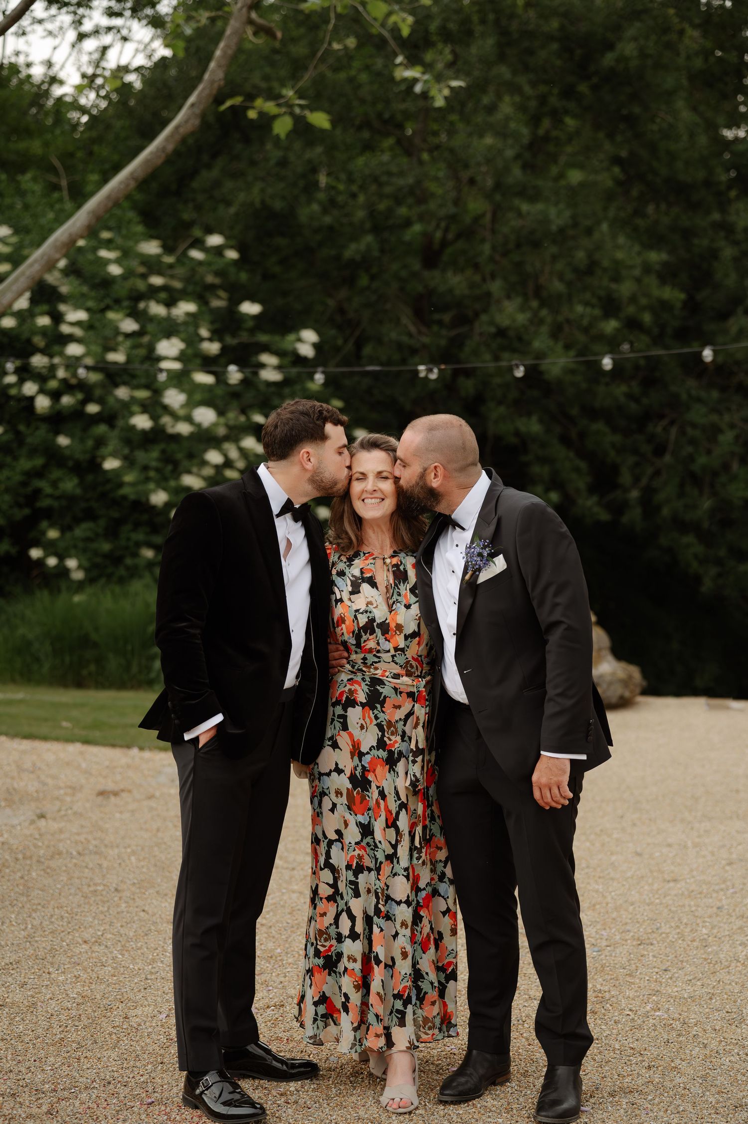 Wedding guests in formal attire gathered outdoors on a gravel path during evening celebrations.