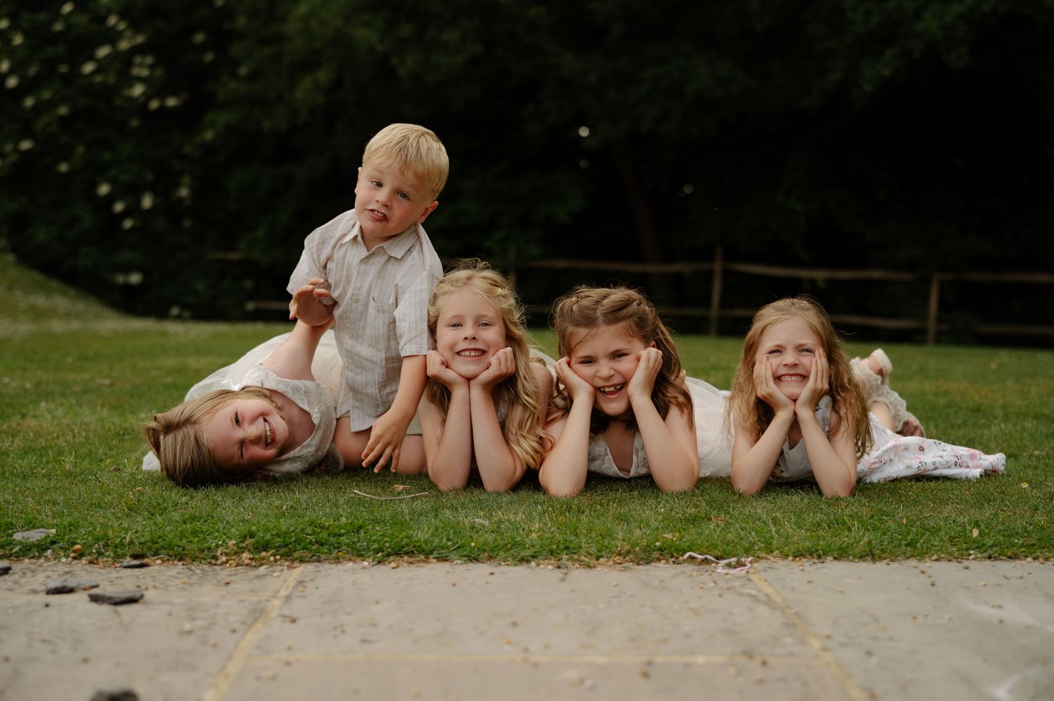 Children lying on grass in a row during outdoor wedding festivities.