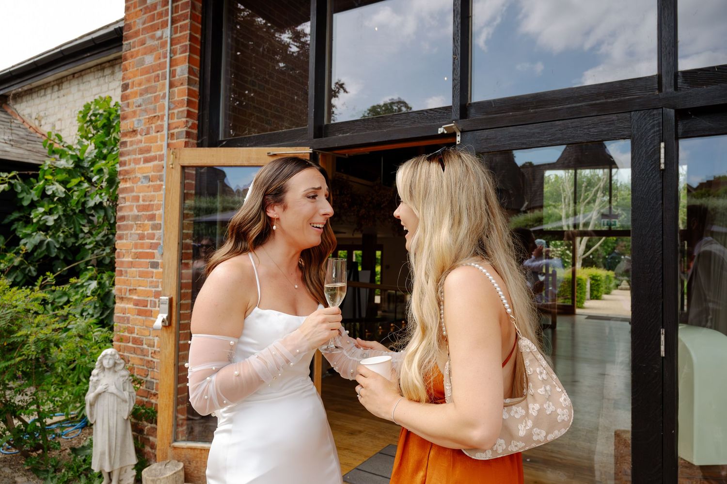 Wedding party members in formal attire celebrate together at a rustic brick venue with large windows.