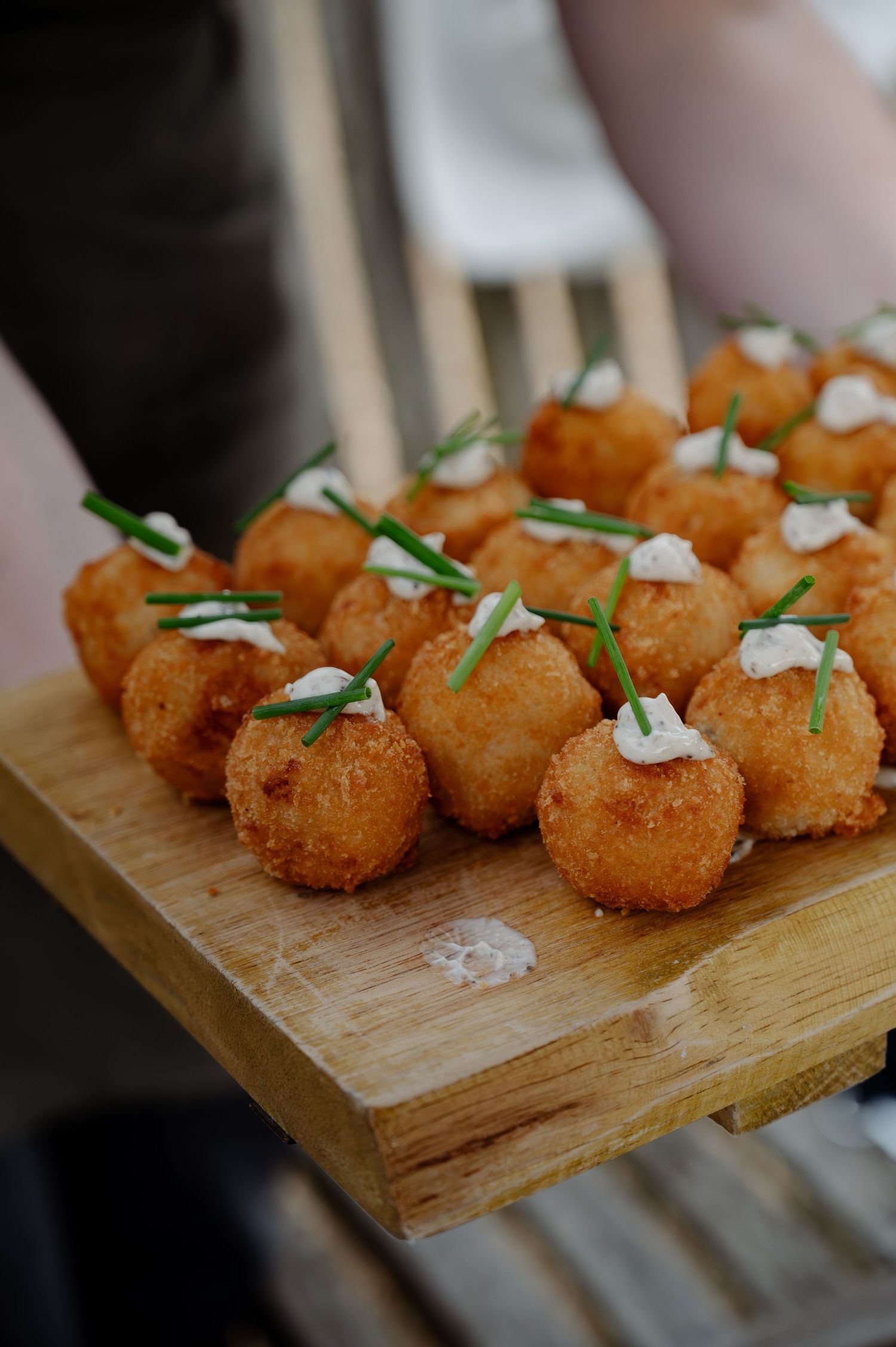Golden fried appetizers garnished with fresh herbs and cream served on a rustic wooden board.
