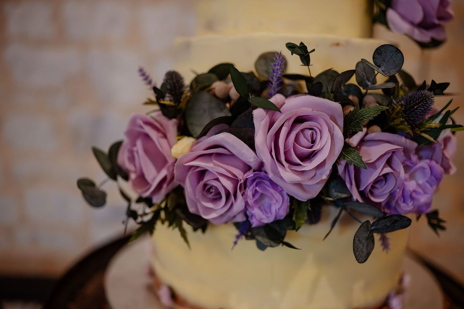 Close-up view of purple roses and floral decorations on an elegant white wedding cake.