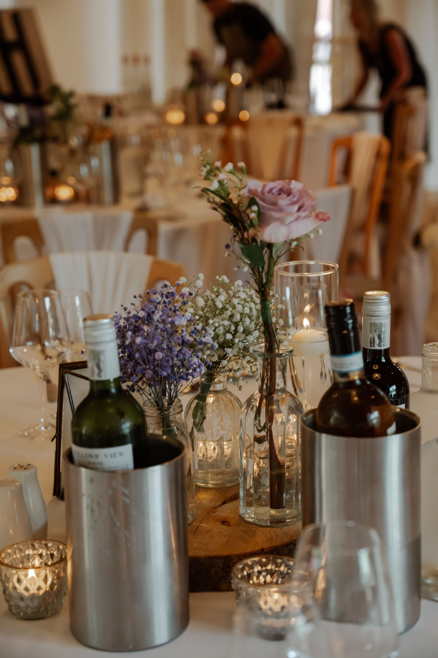 Elegant wedding reception table with silver vases, candles, and delicate floral arrangements in a white room.