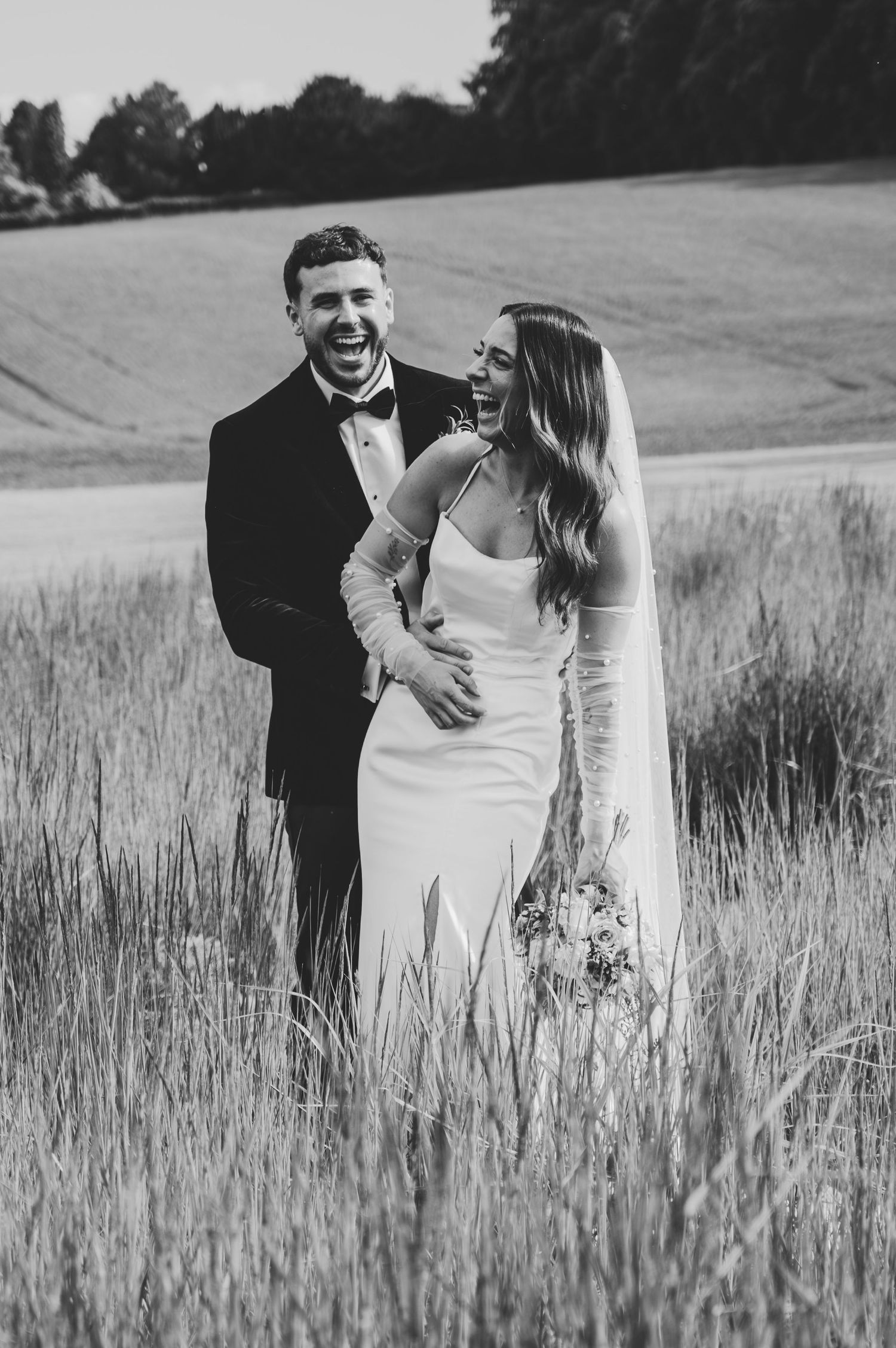 Black and white photo of a couple embracing in a serene wheat field.