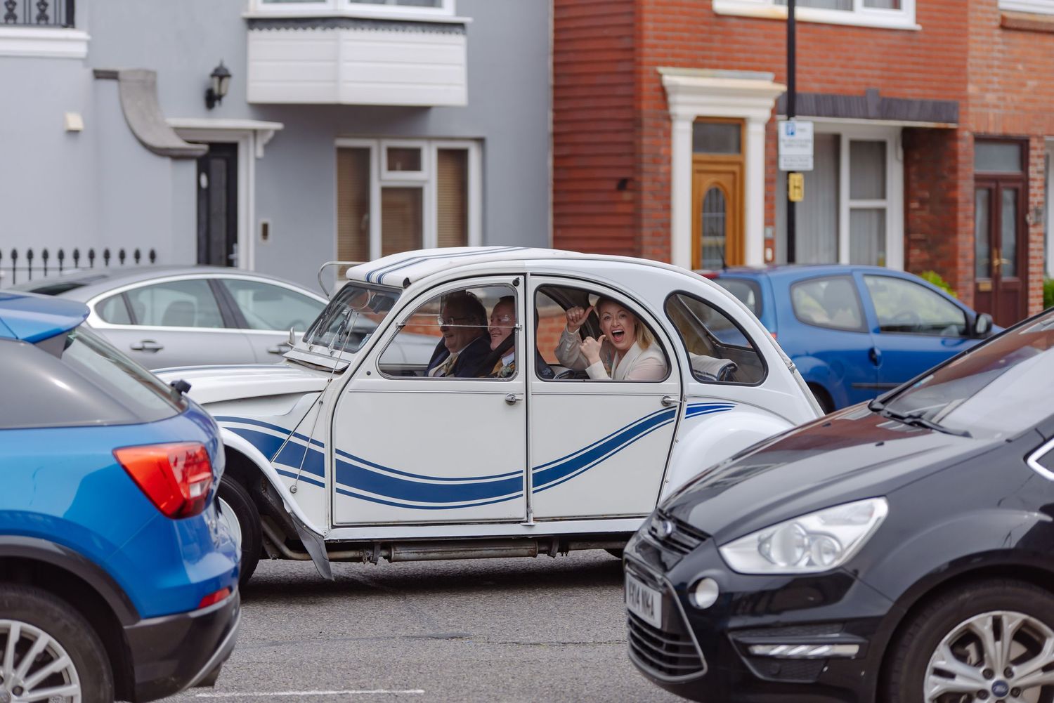 Vintage white Citroen 2CV car parked between modern vehicles on a residential street.