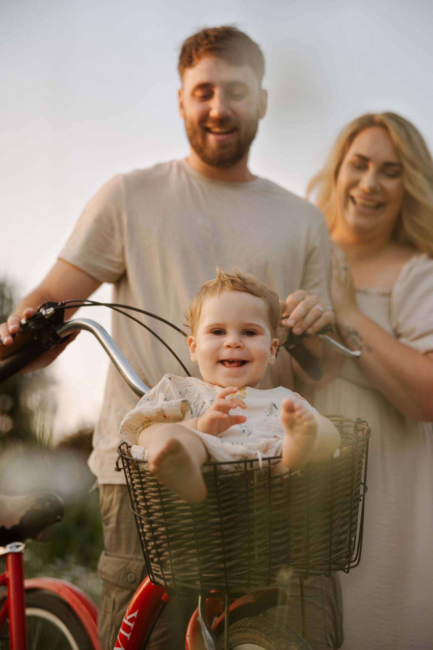 Happy baby sitting in a bicycle basket with smiling parents enjoying a sunny outdoor family bike ride.