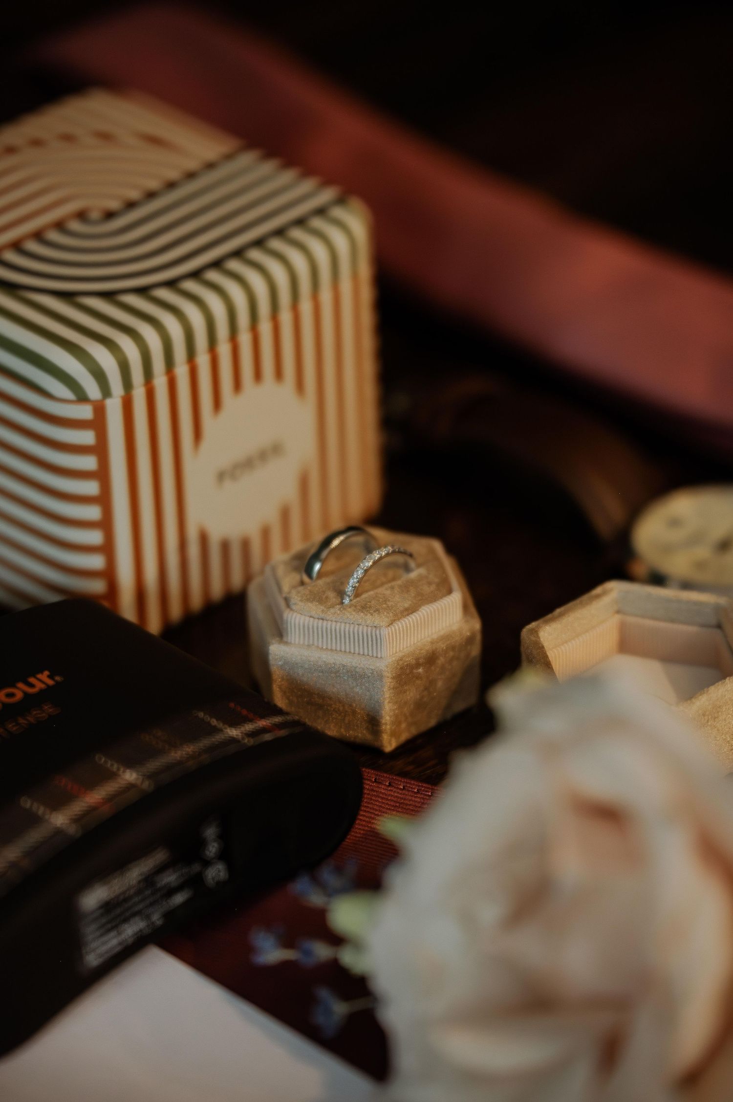 A vintage-style striped gift box and small hexagonal jewelry case sit beside a delicate white rose in moody lighting.