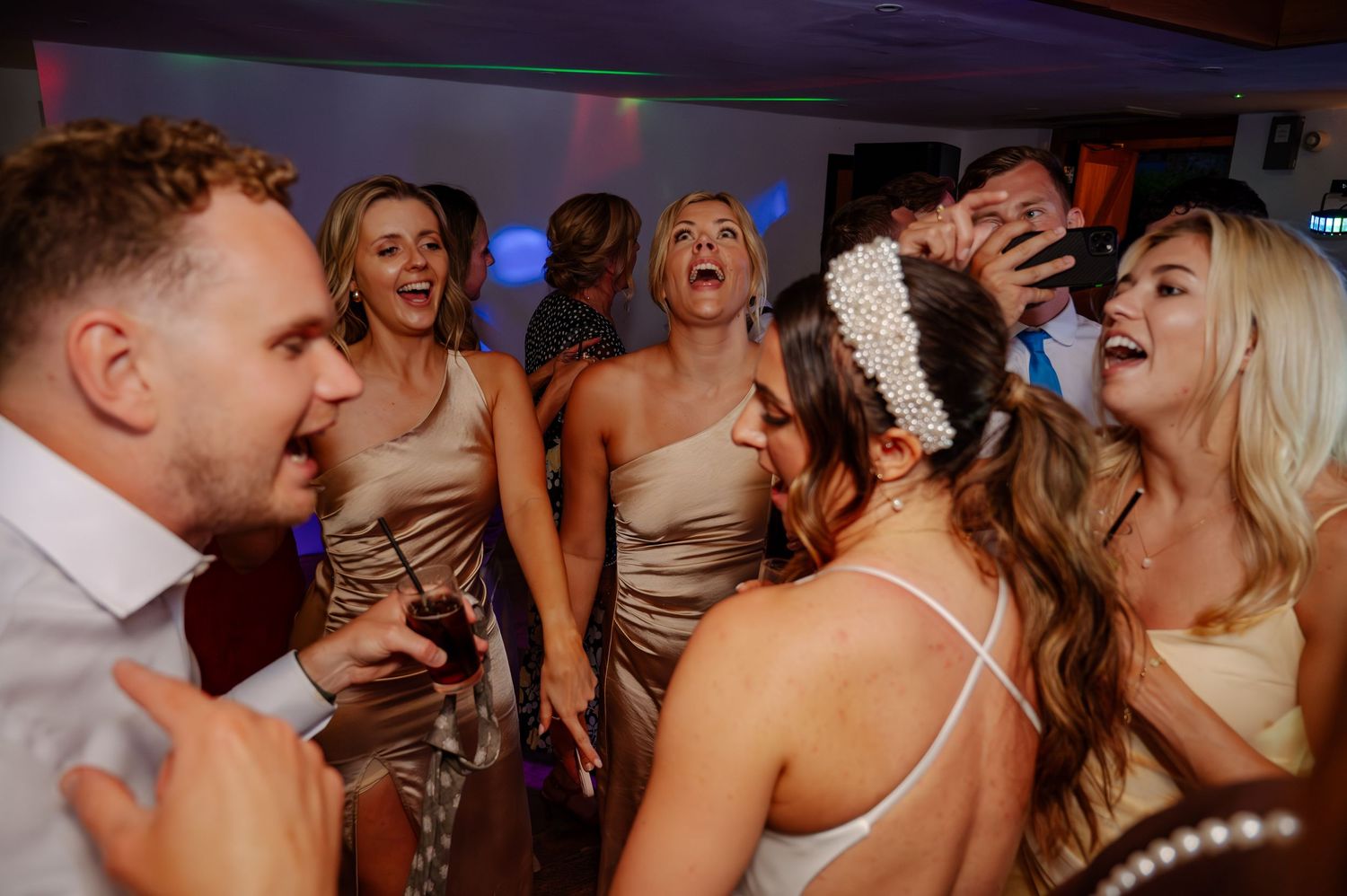Energetic crowd of wedding guests dancing and celebrating on a dark dance floor.