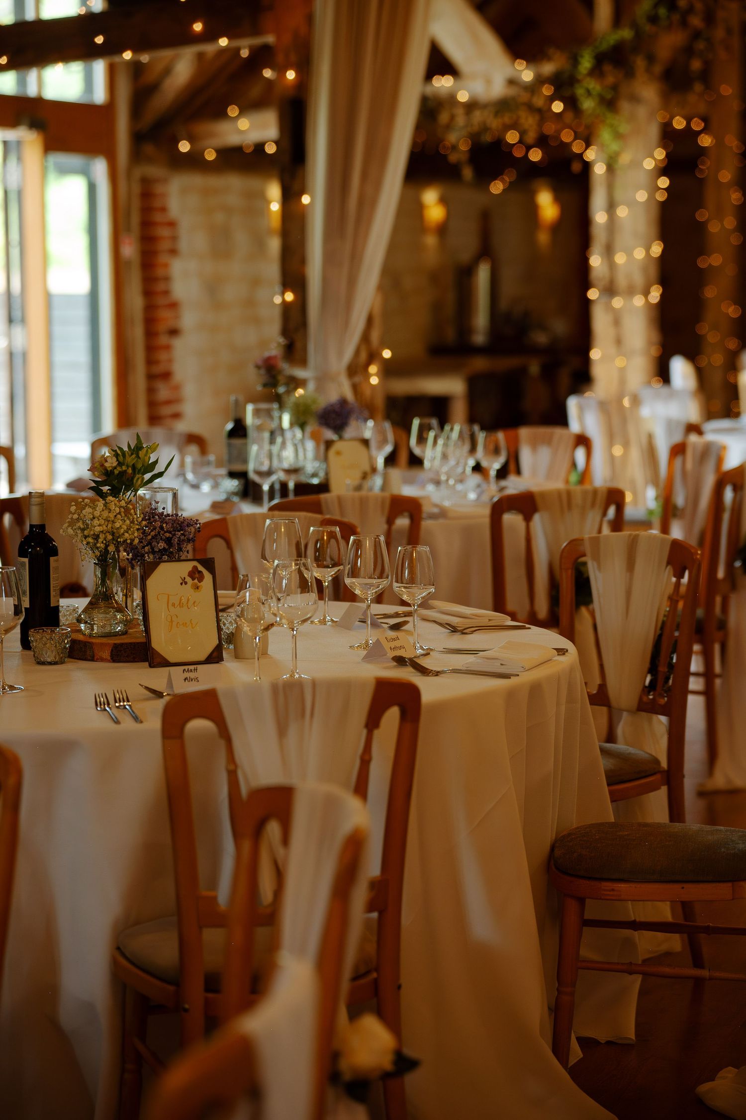Elegant wedding reception venue with round tables set with white linens and glowing string lights overhead.