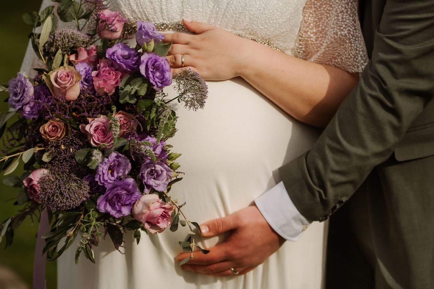 Wedding couple holds a romantic purple and pink floral bouquet with roses and mixed flowers against a light background.