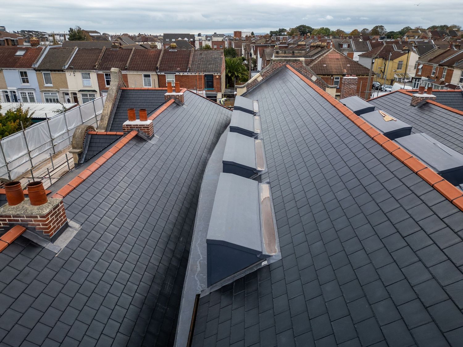 Panoramic view of residential rooftops with solar panels installed under cloudy skies in an urban neighborhood.