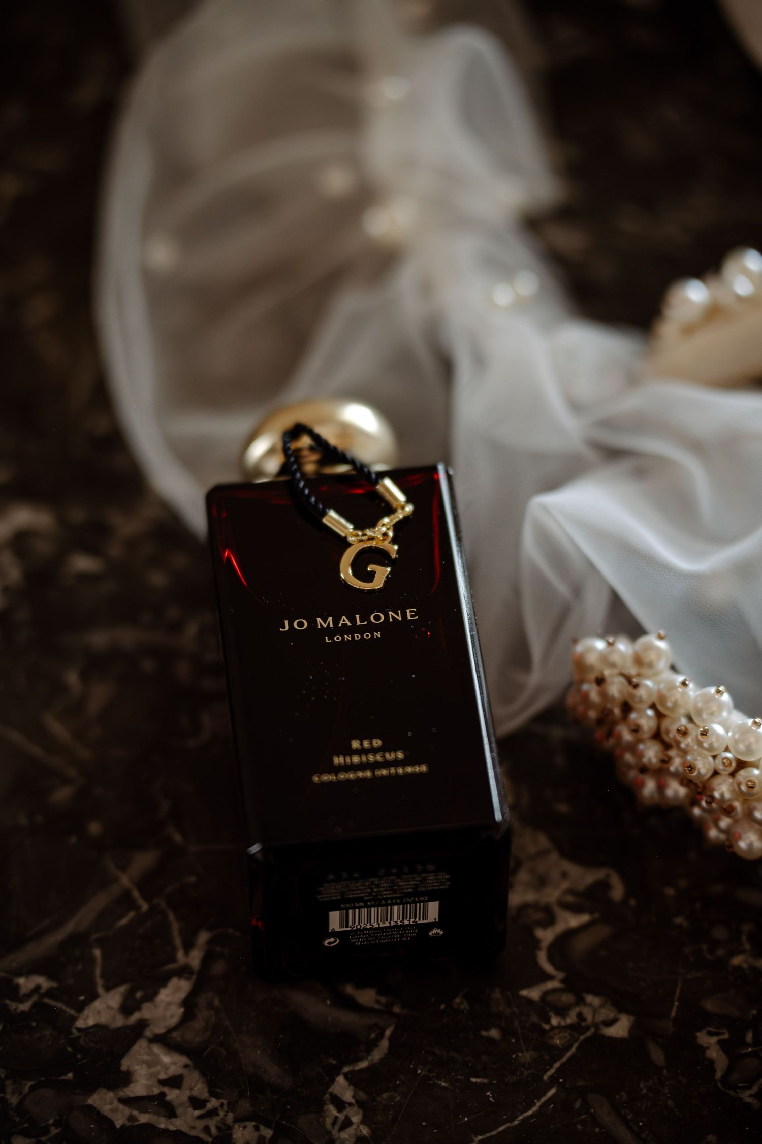 Jo Malone perfume bottle and jewelry details photographed on dark textured surface with soft lighting.