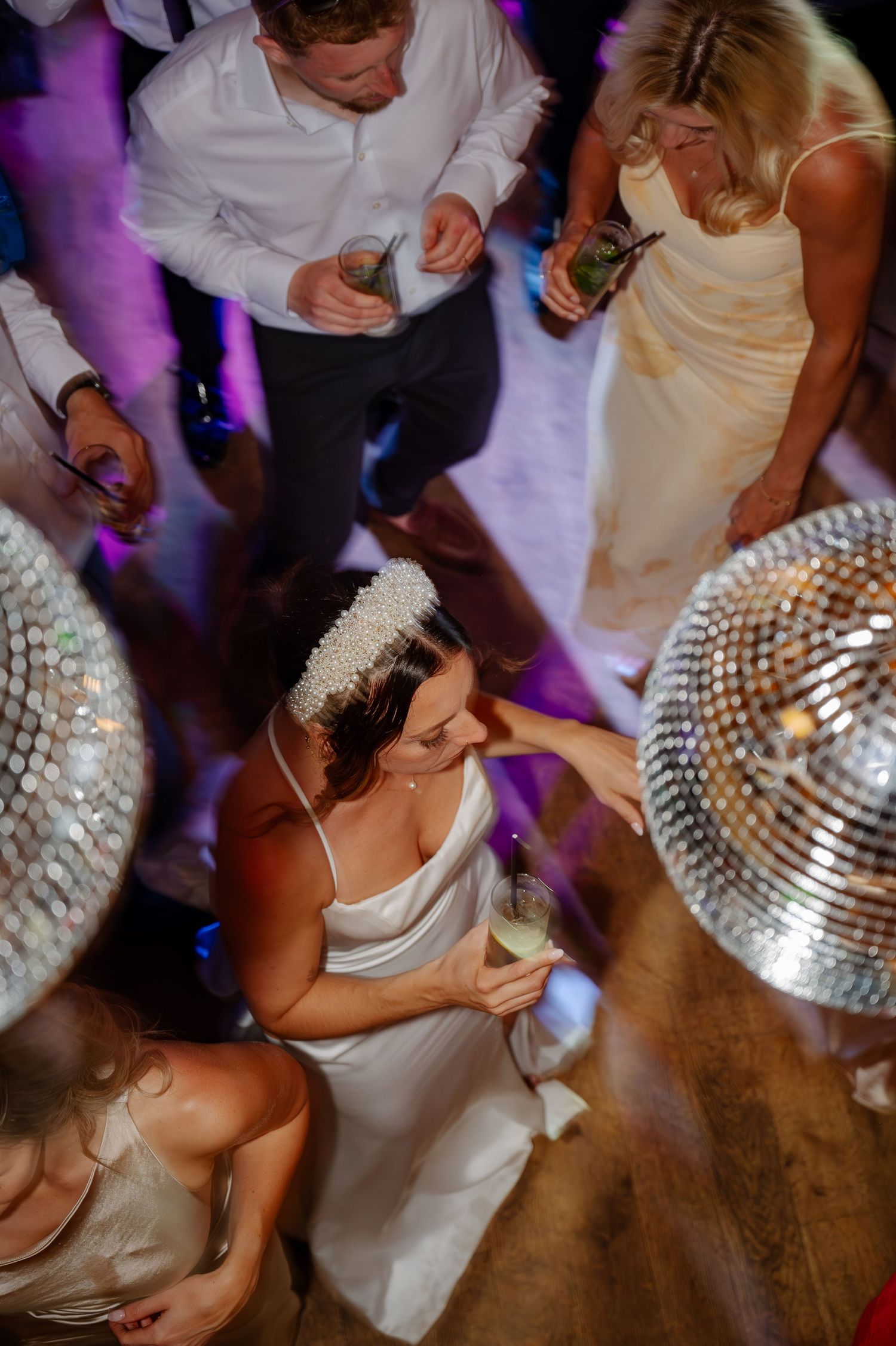Wedding reception dance floor with disco ball casting purple lighting and guests dancing.