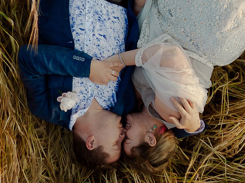 Romantic overhead view of couple in formal attire lying in grass field.