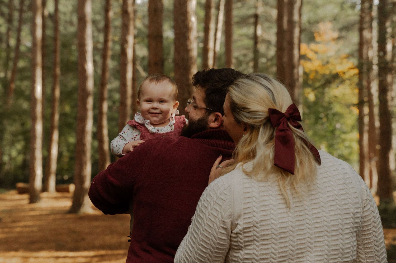 Family enjoying a playful autumn photoshoot in a wooded park with golden sunlight filtering through trees.