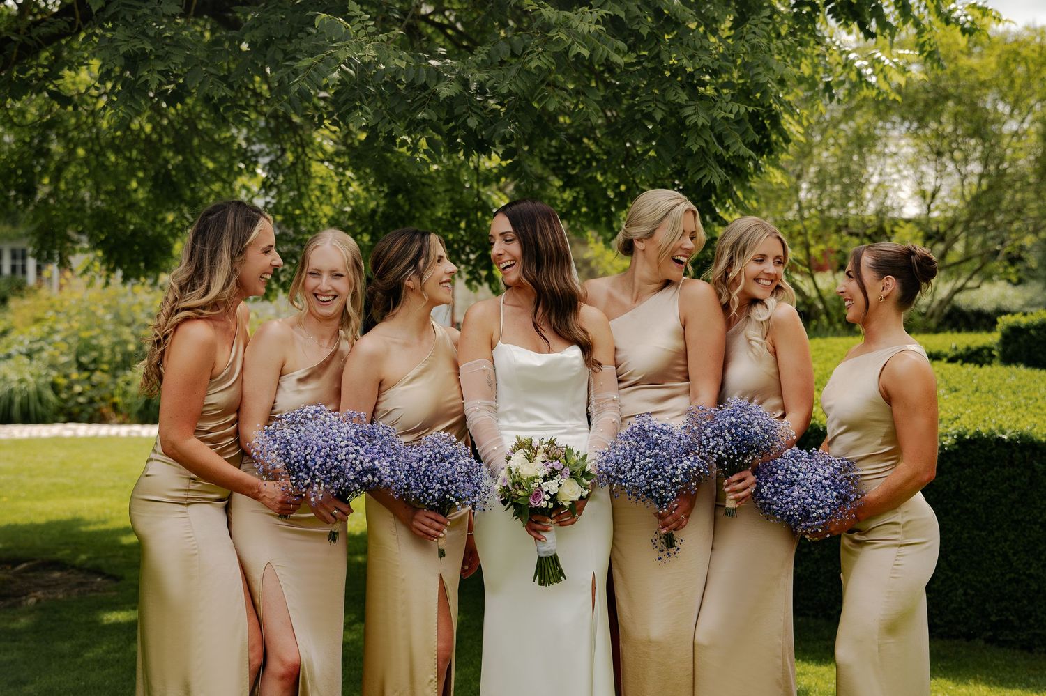 Bridesmaids in pastel dresses holding purple hydrangea bouquets in a garden setting.