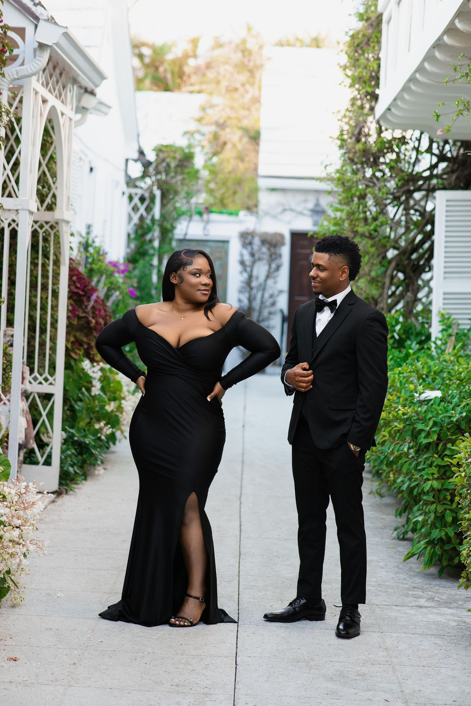 Couple in matching black formal wear posing in a garden courtyard setting.
