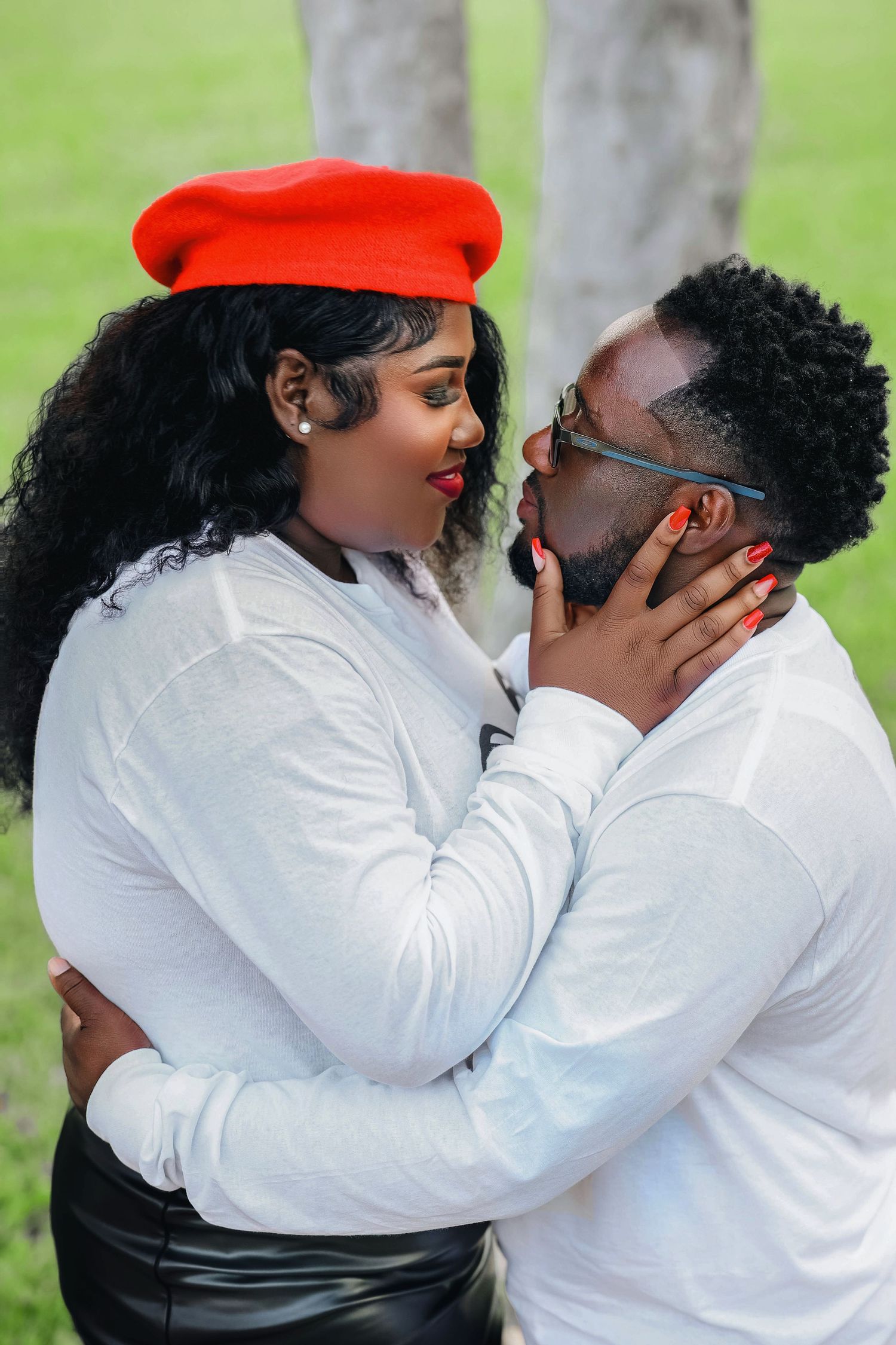 Romantic couple in white tops and red accents sharing an intimate moment in a park.