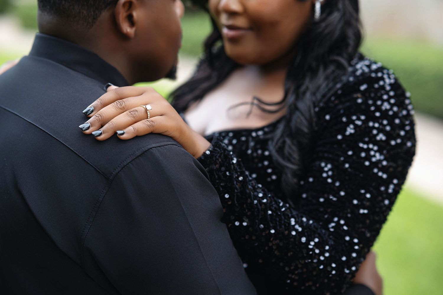 Close-up of woman's hand with engagement ring resting on man's shoulder during couples photo session.