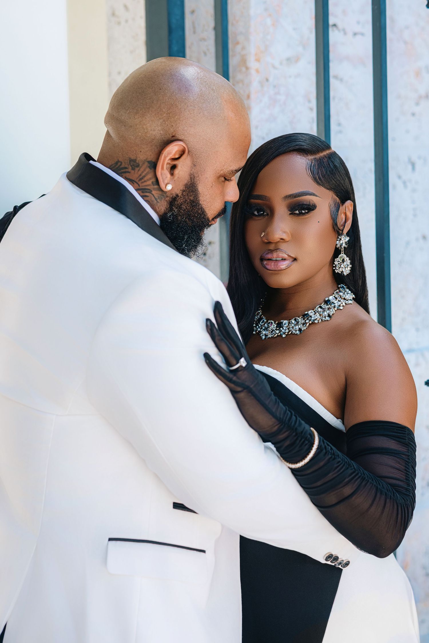 Elegant couple in black and white formal wear share an intimate moment, woman wearing diamond jewelry and black gloves.