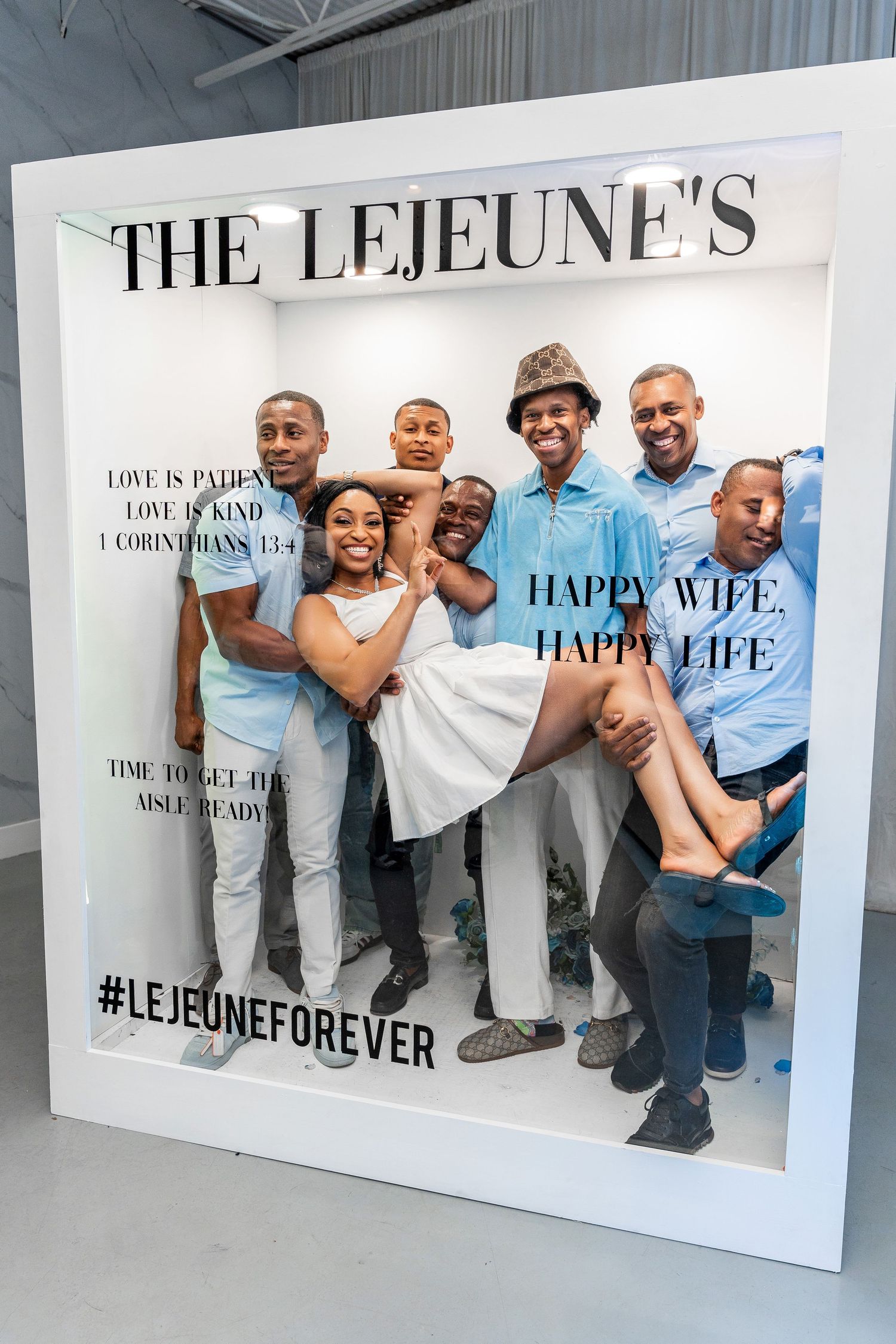 Bride carried by six men poses inside The Lejeune's Happy Wife Happy Life wedding photo booth frame.