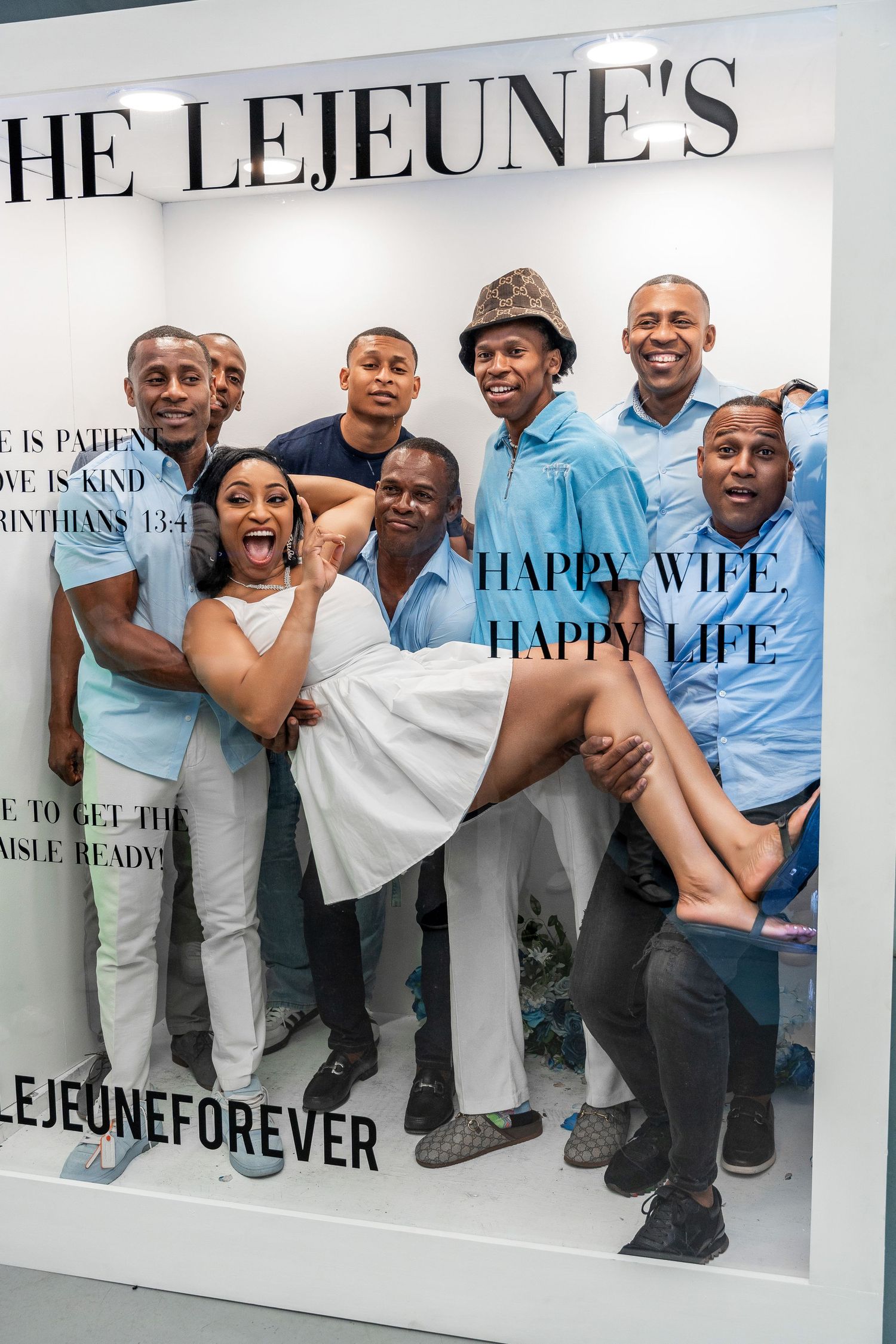 A group of men carry a smiling woman in a white dress inside The Lejeunes photo frame display.
