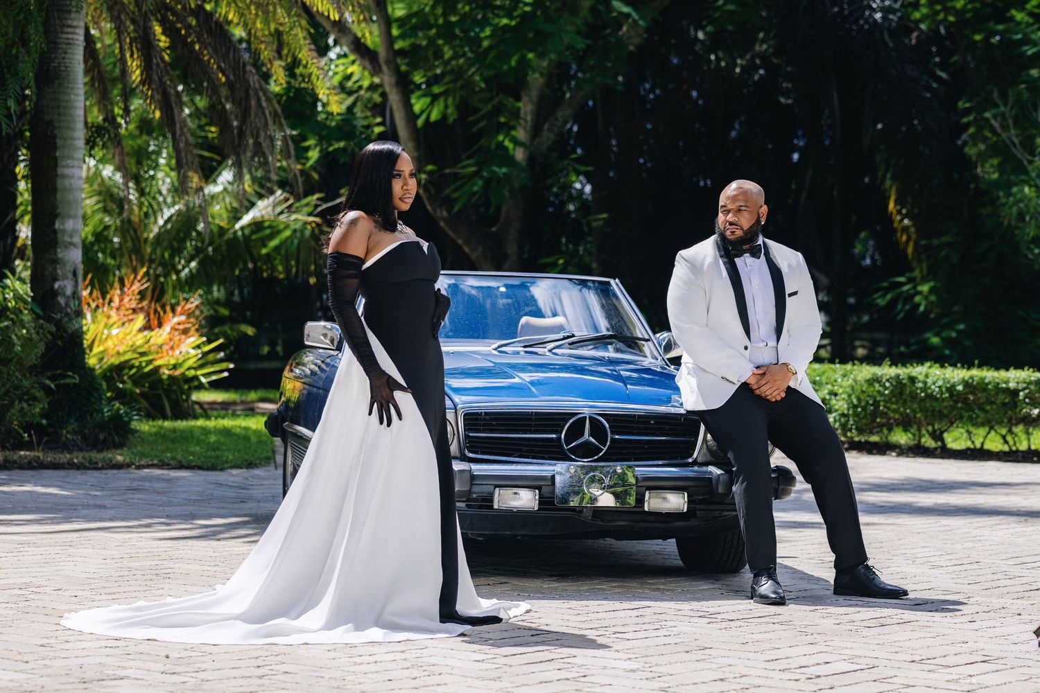 Elegant couple in black and white formal attire pose beside a classic vintage Mercedes-Benz convertible outdoors.