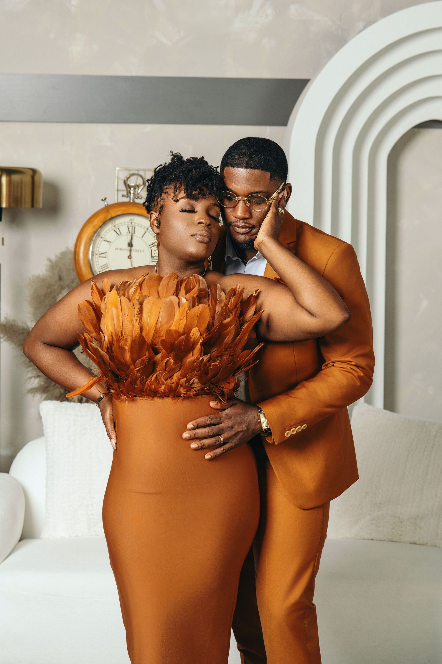 Couple in burnt orange outfits sharing an intimate embrace in a sophisticated white room.