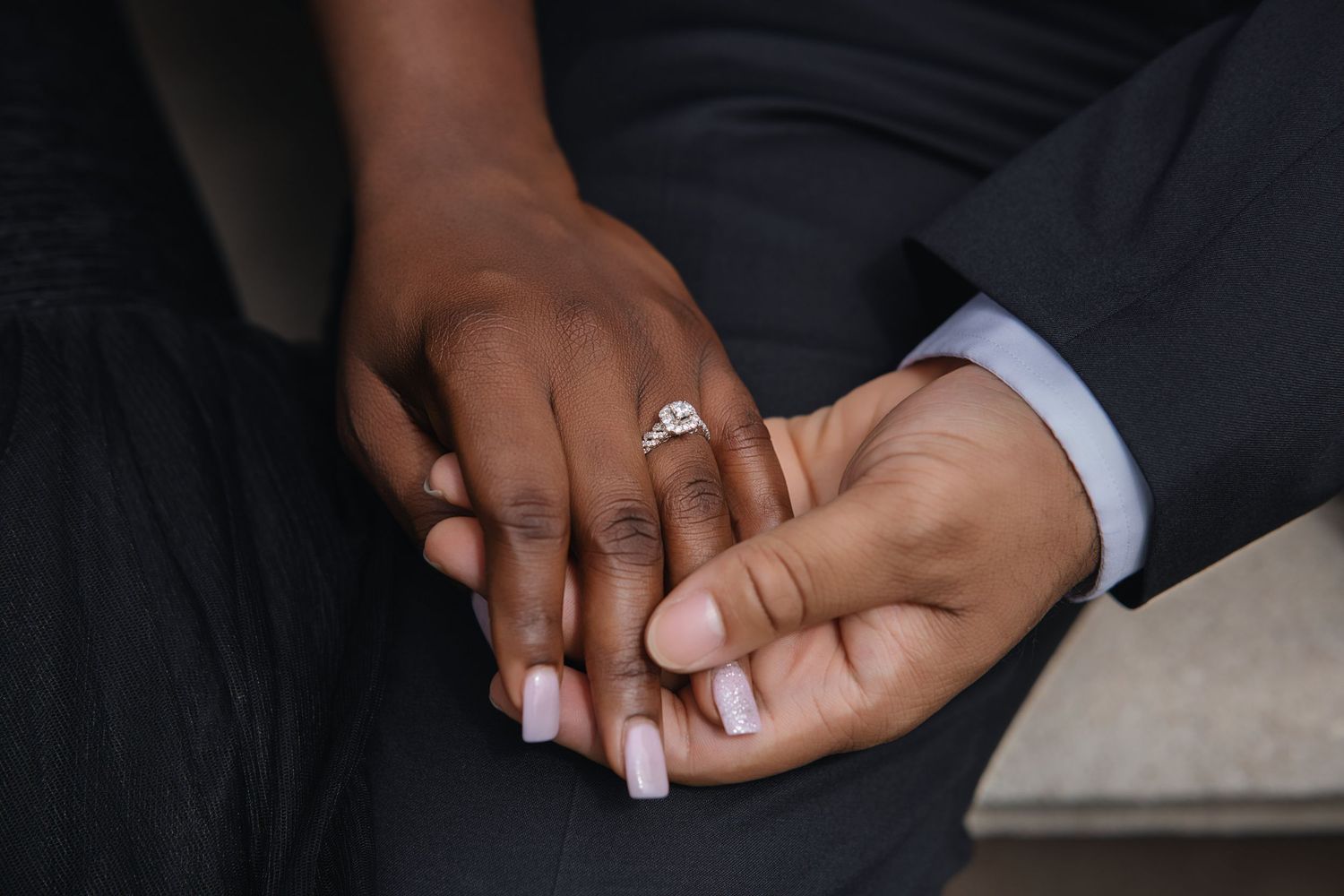 Close-up of couple holding hands displaying a sparkling diamond engagement ring with manicured nails.