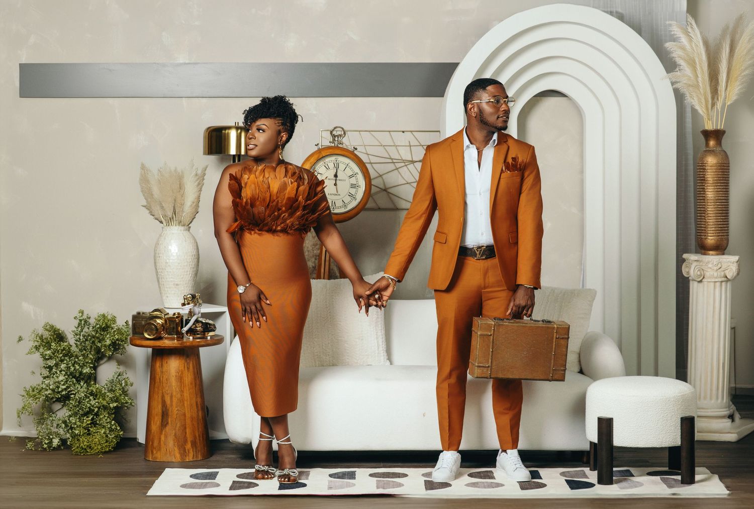 Couple holding hands in coordinating burnt orange outfits in stylish modern interior setting.