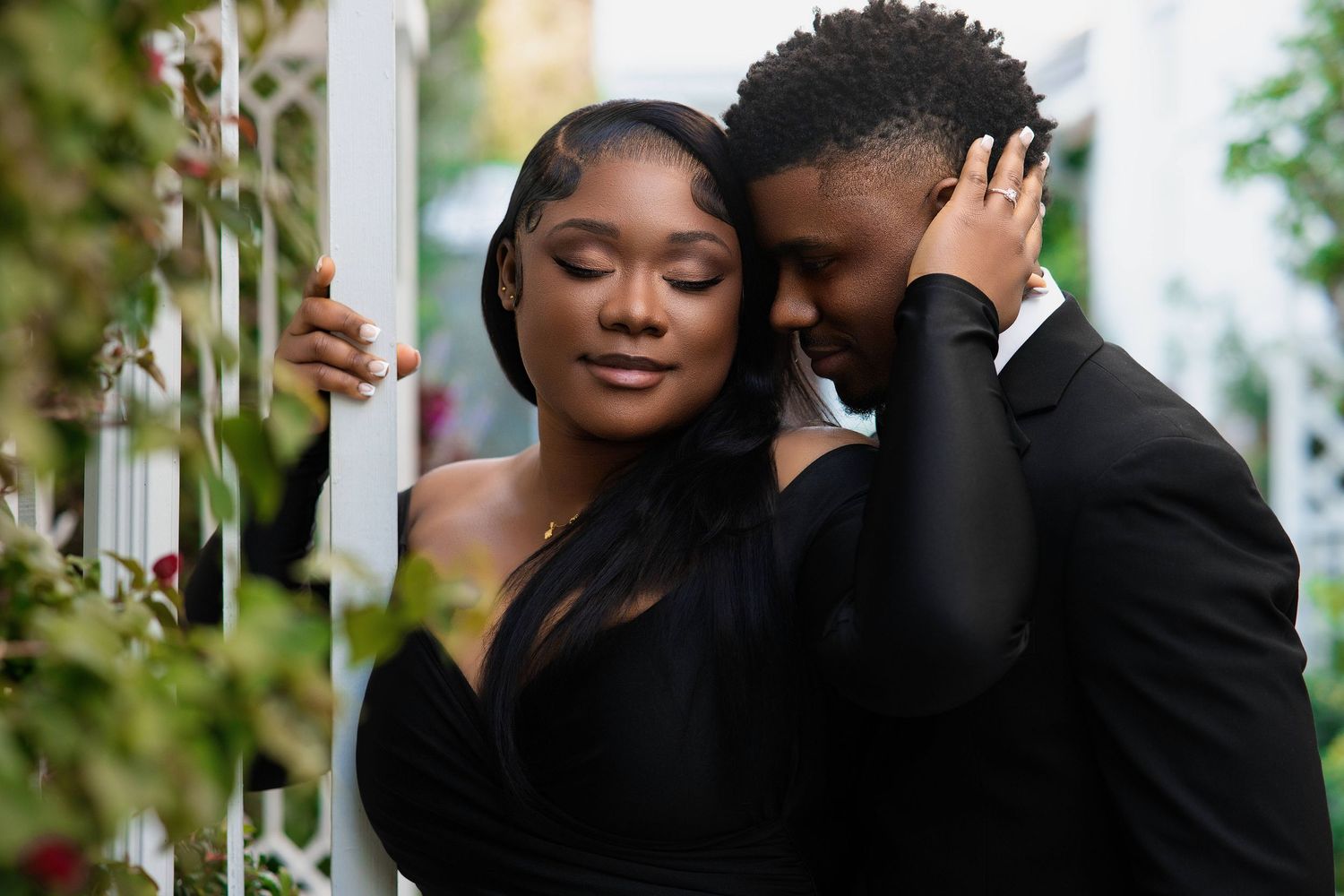 Romantic Black couple in matching black formal wear sharing a tender embrace outdoors.