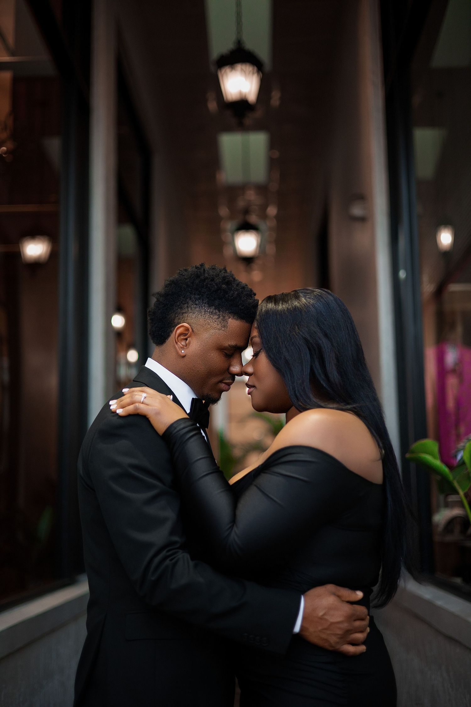 Elegant Black couple in formal black attire sharing an intimate moment under warm lights.
