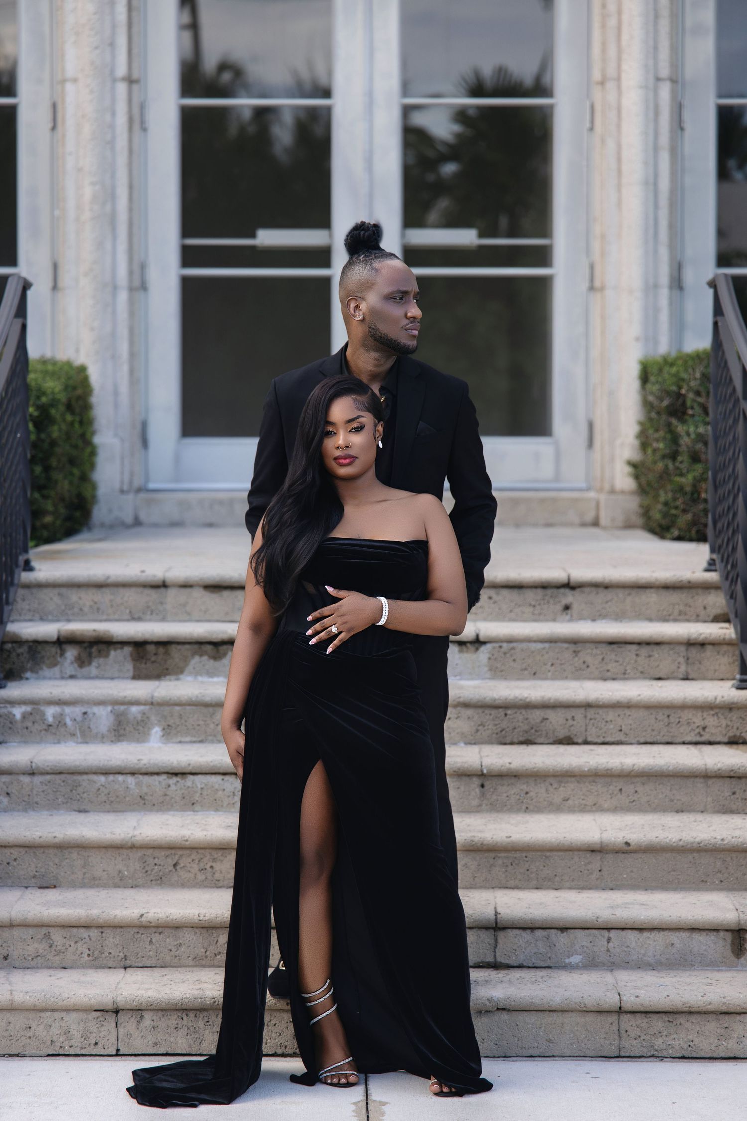 Couple in black velvet formal wear posing intimately on marble building steps.