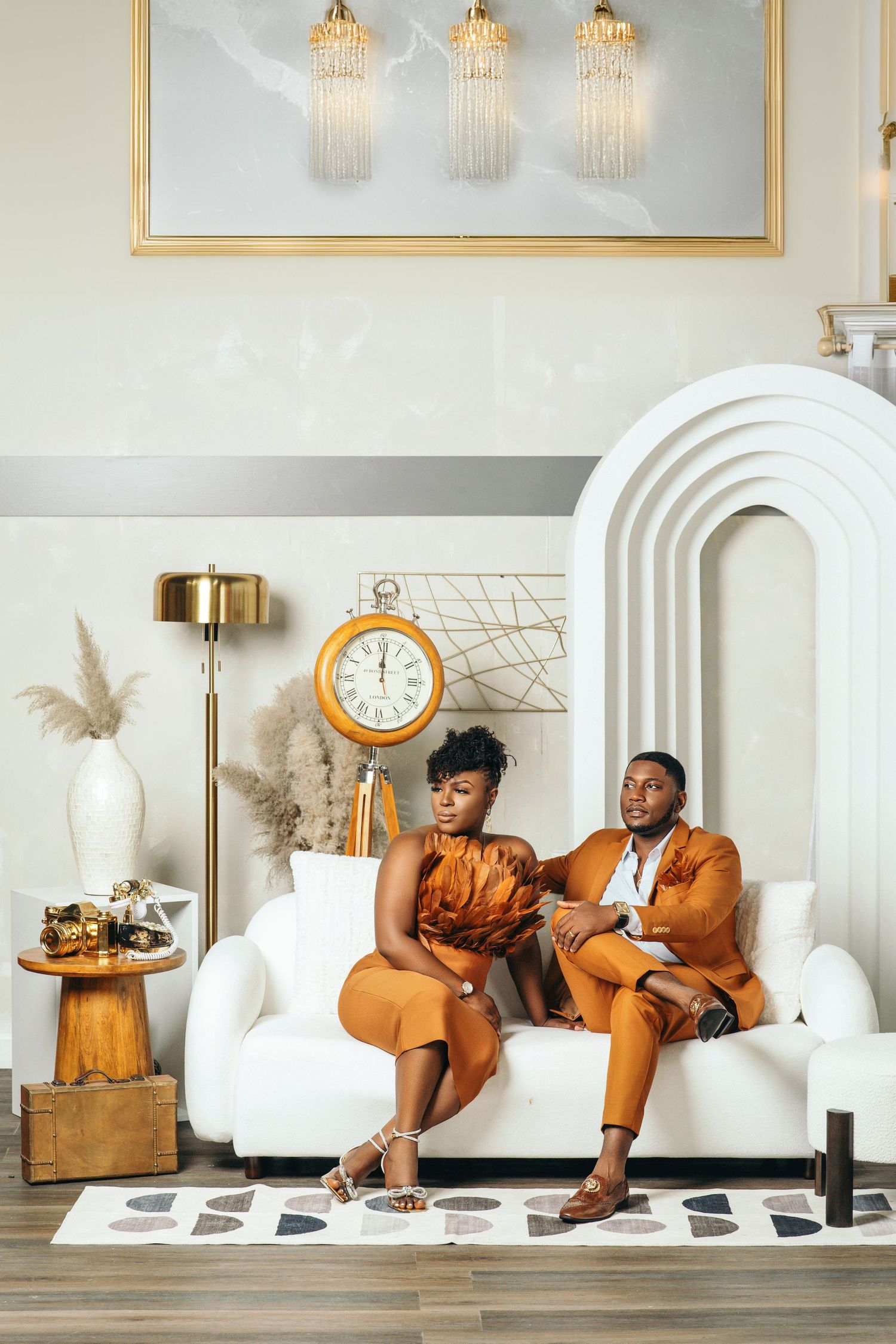 Stylish couple in matching burnt orange outfits seated on a white sofa in elegant decor.