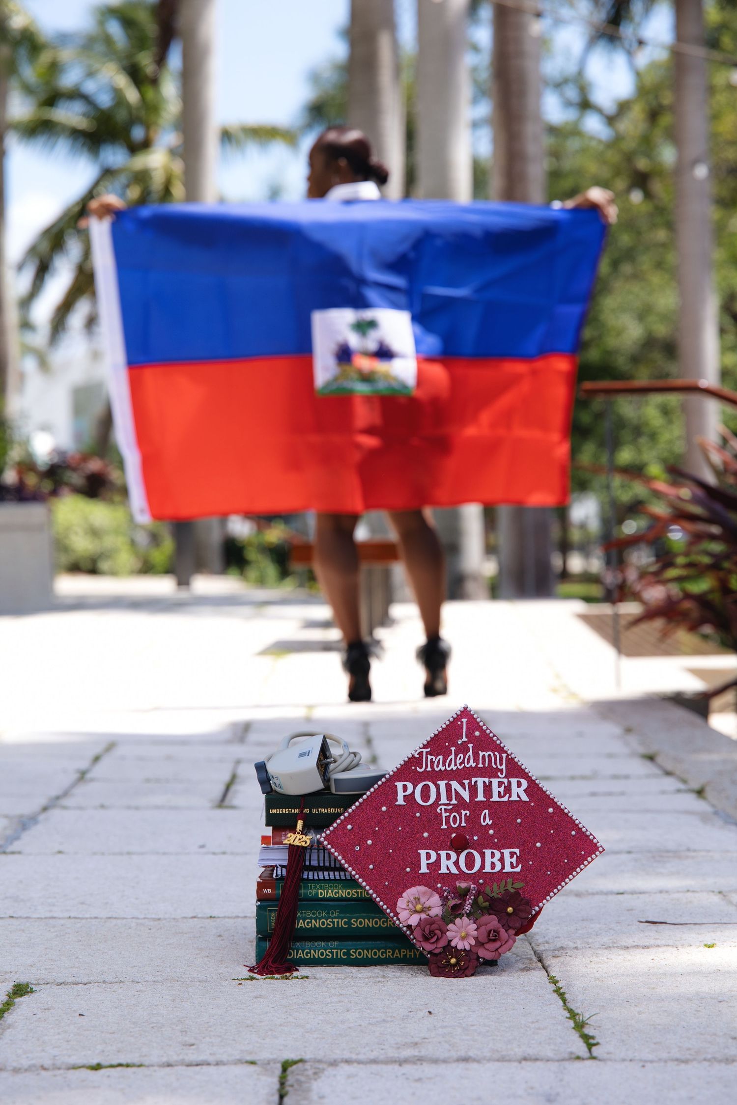 Haitian flag held proudly outdoors with a decorated graduation cap reading I Traded My Pointer for a Probe in foreground.