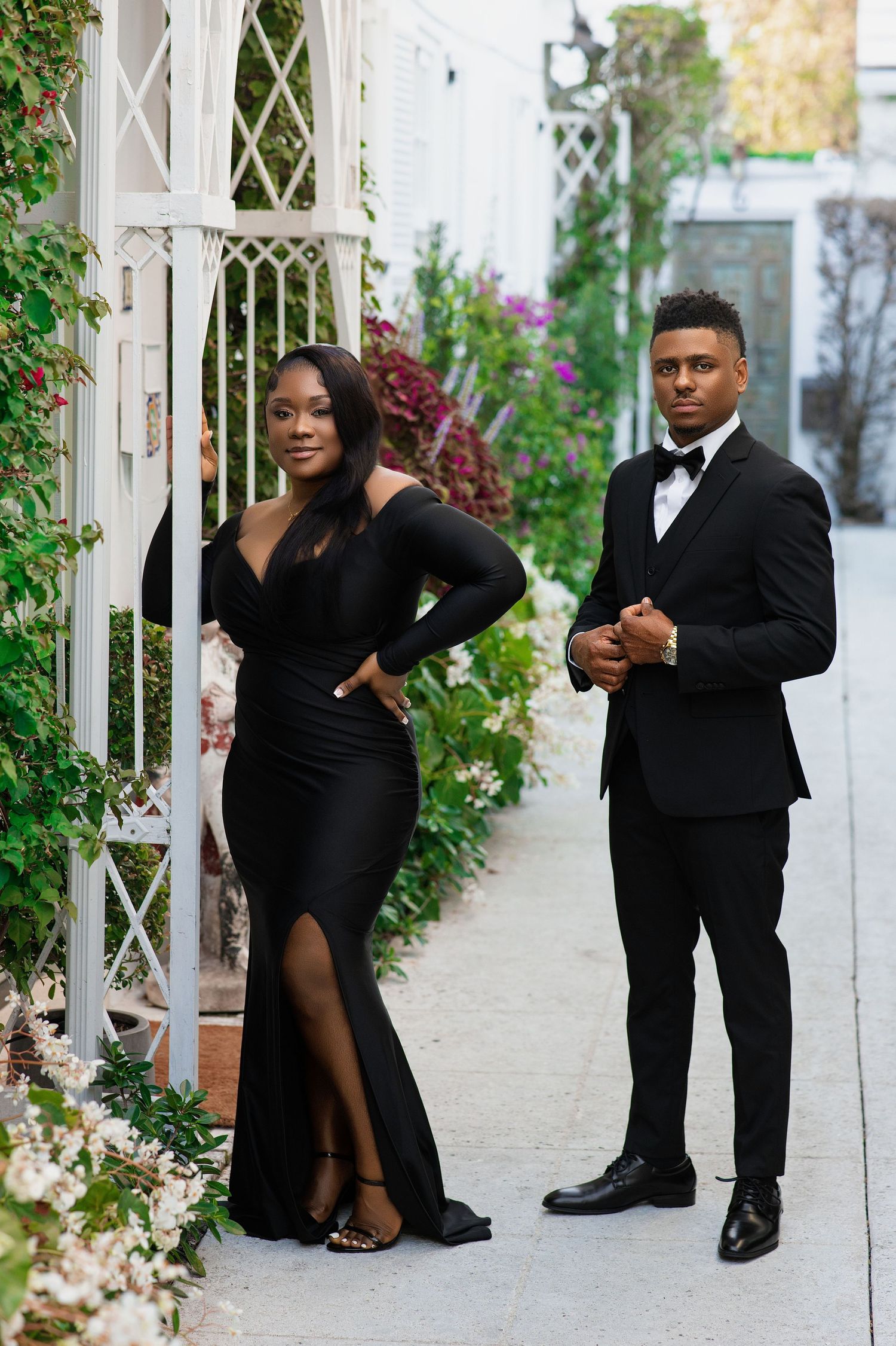 Stunning Black couple posing in coordinated black formal outfits among lush garden florals.