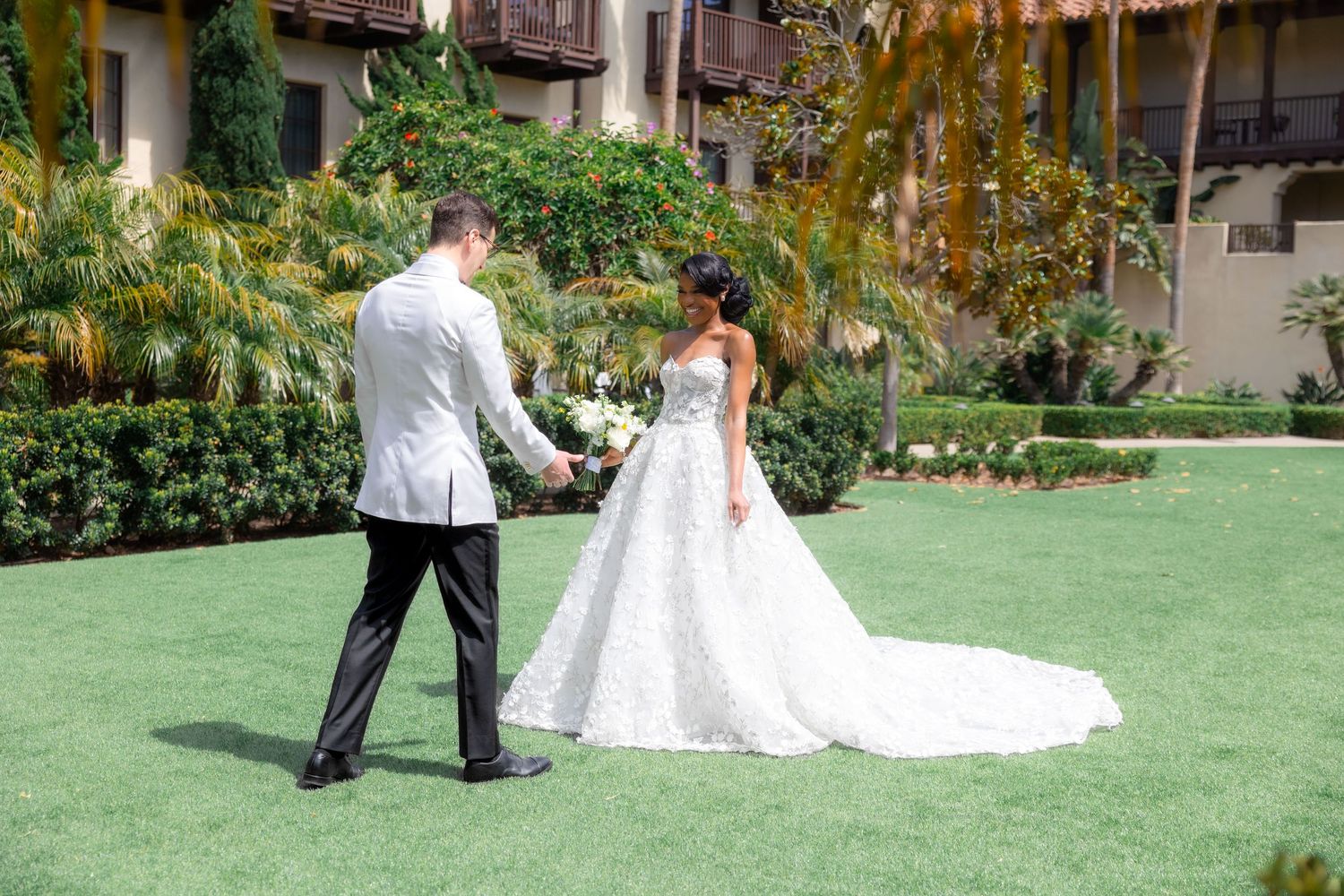 Bride and groom share a first look moment on lush green lawn at elegant outdoor wedding venue.