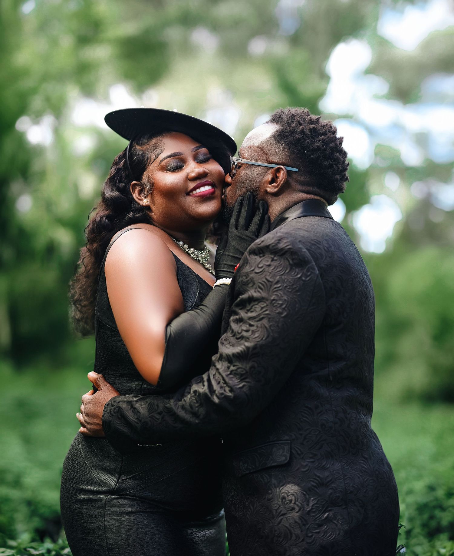 Couple sharing a tender kiss outdoors surrounded by lush green foliage.