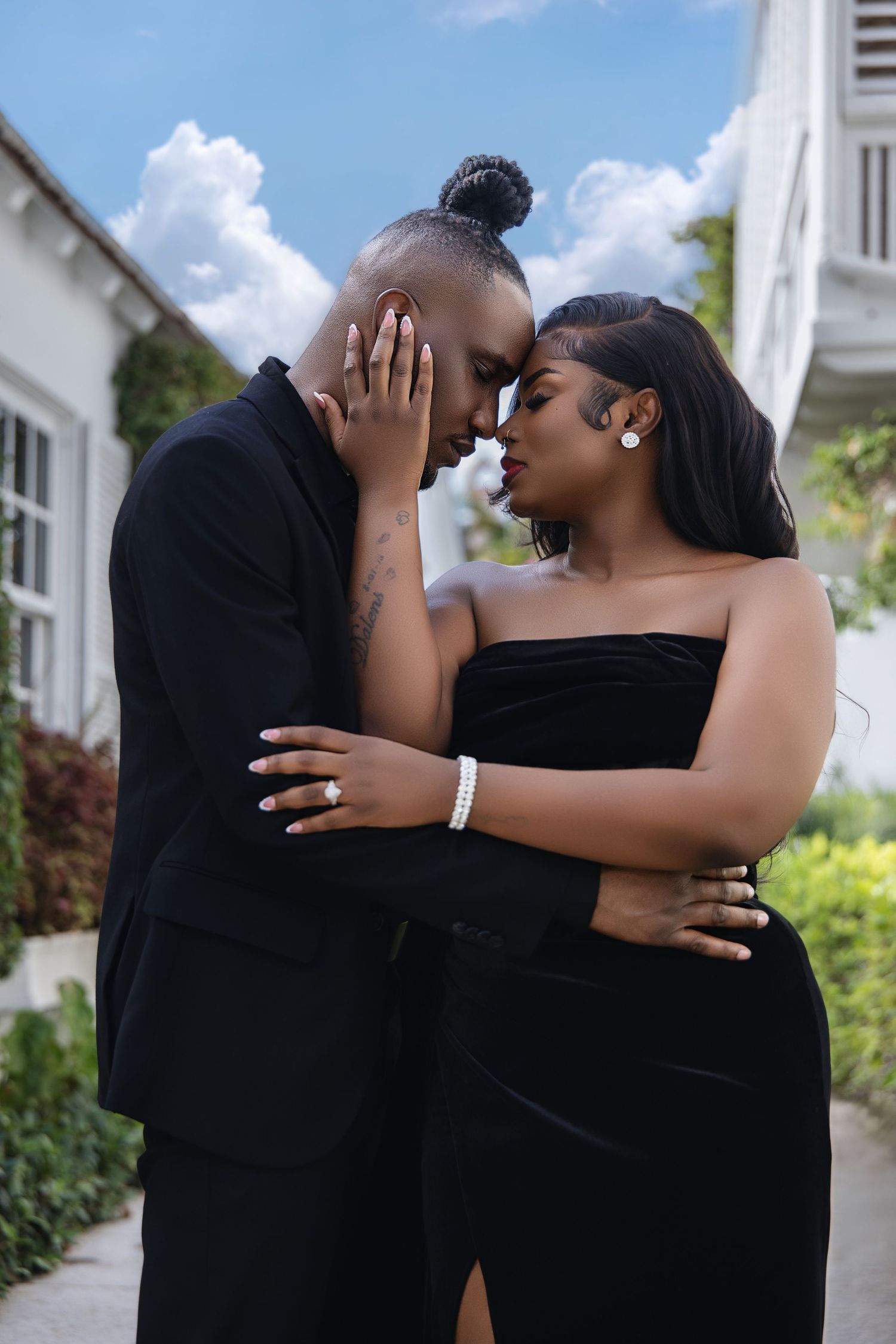 Romantic couple in matching black formal wear sharing an intimate moment outdoors.