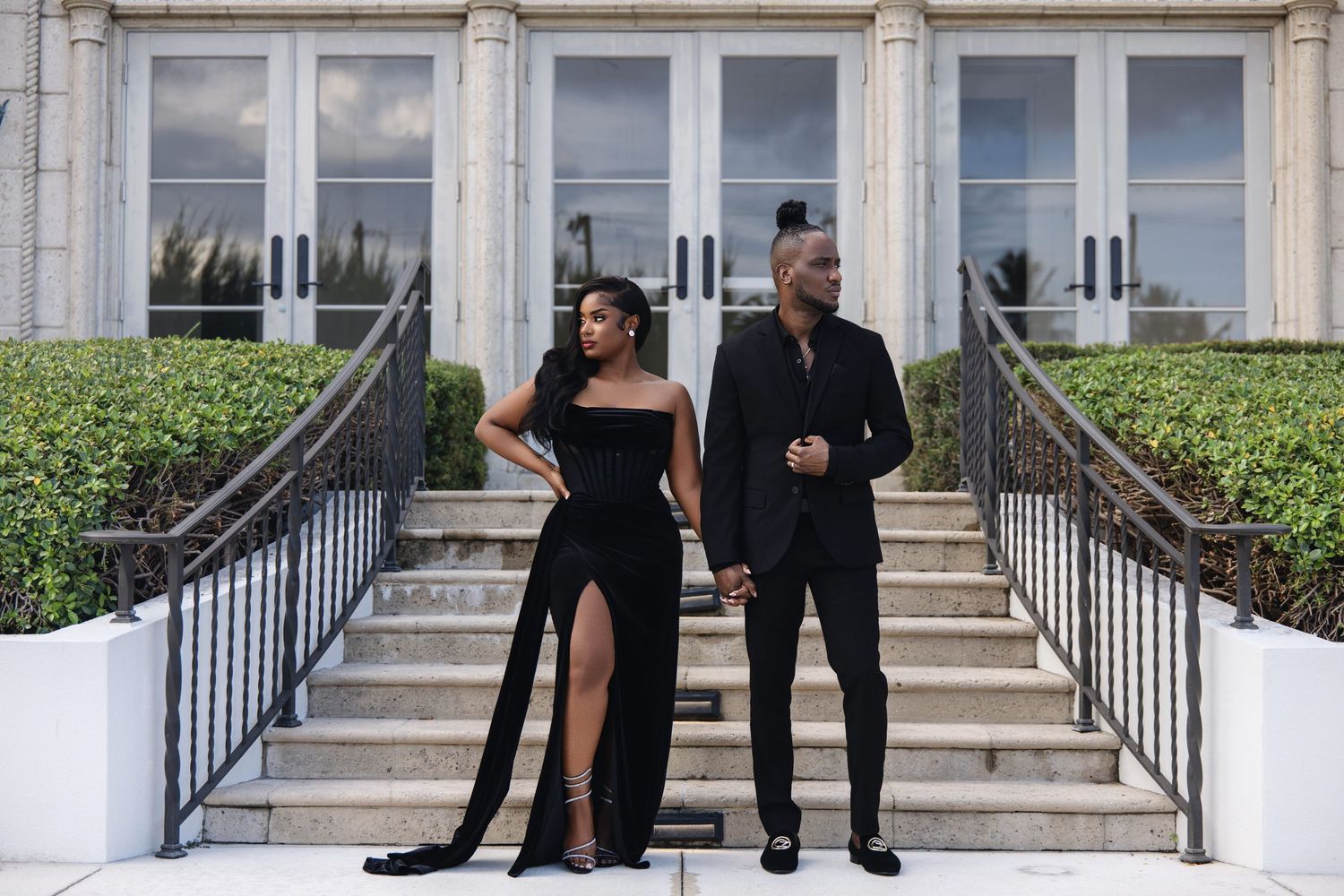 Couple dressed in black formalwear posing apart on wide outdoor staircase steps.