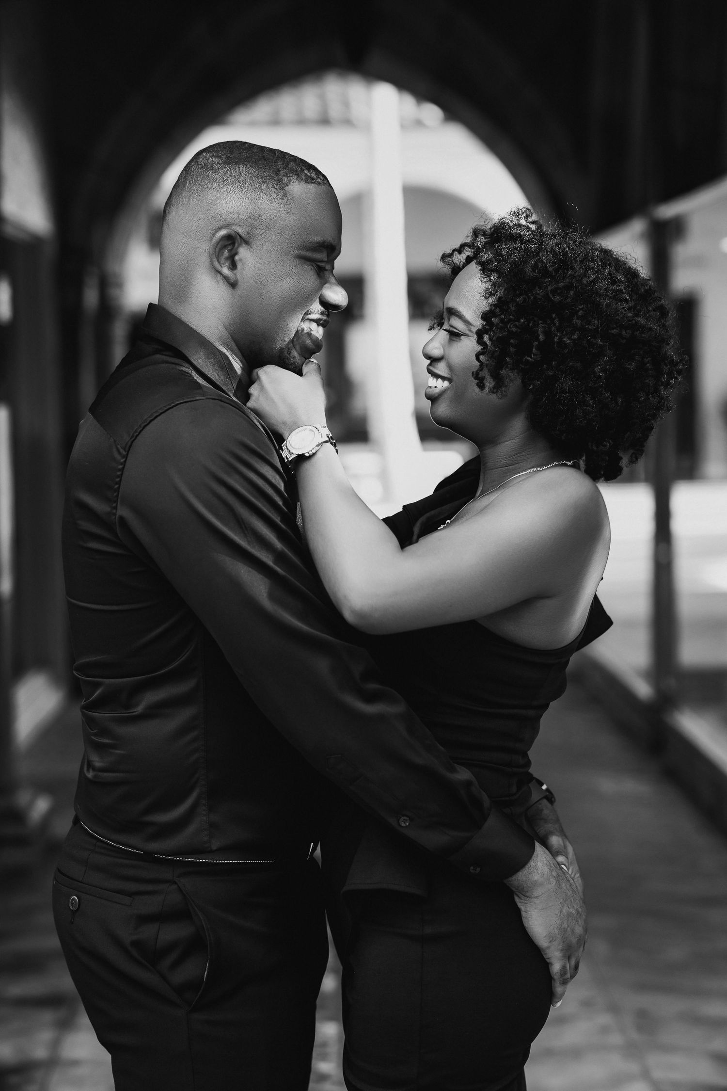 Black and white photo of a joyful couple laughing and embracing under an arched corridor.
