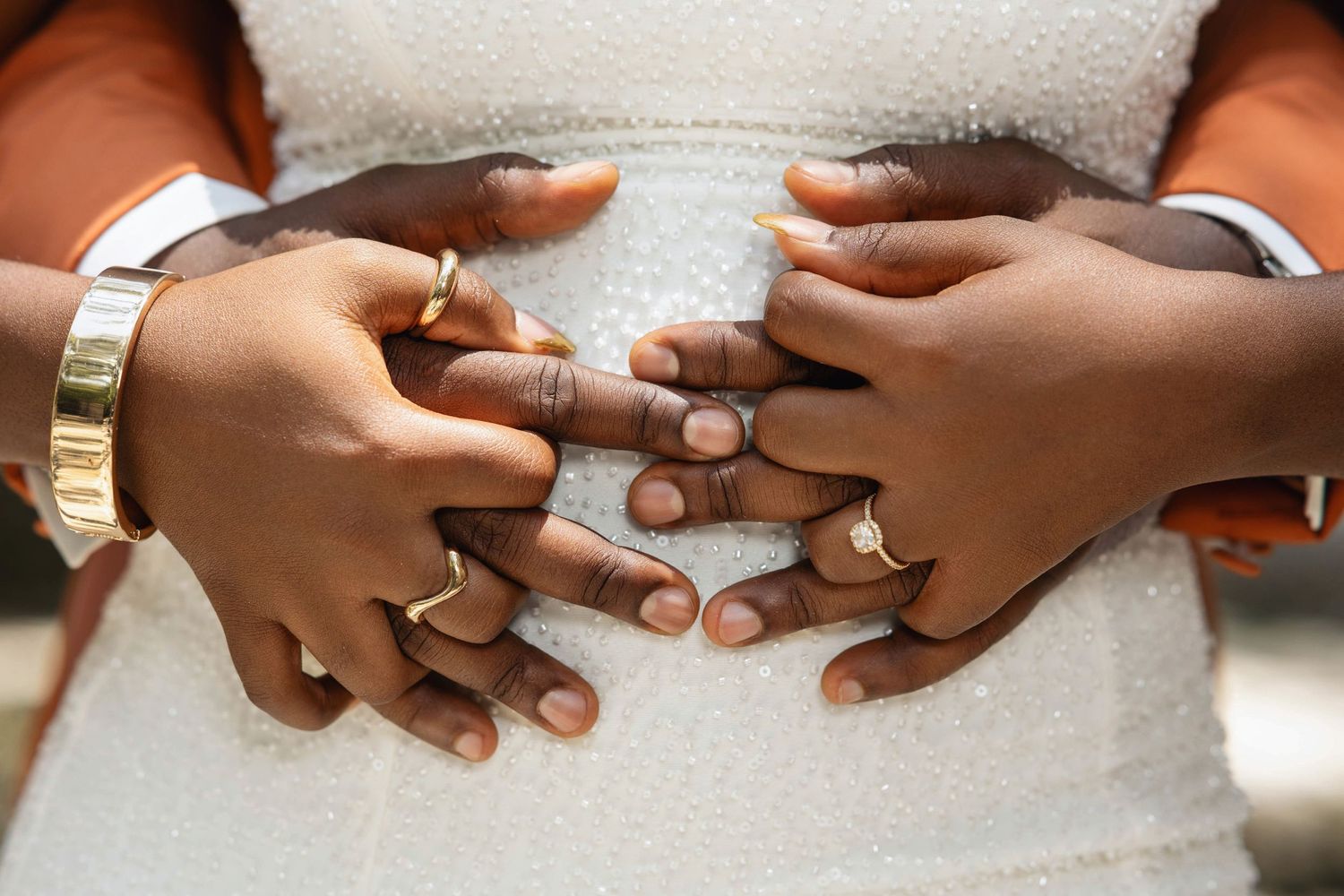 Close-up of engaged couples hands intertwined showing diamond engagement ring on white dress.