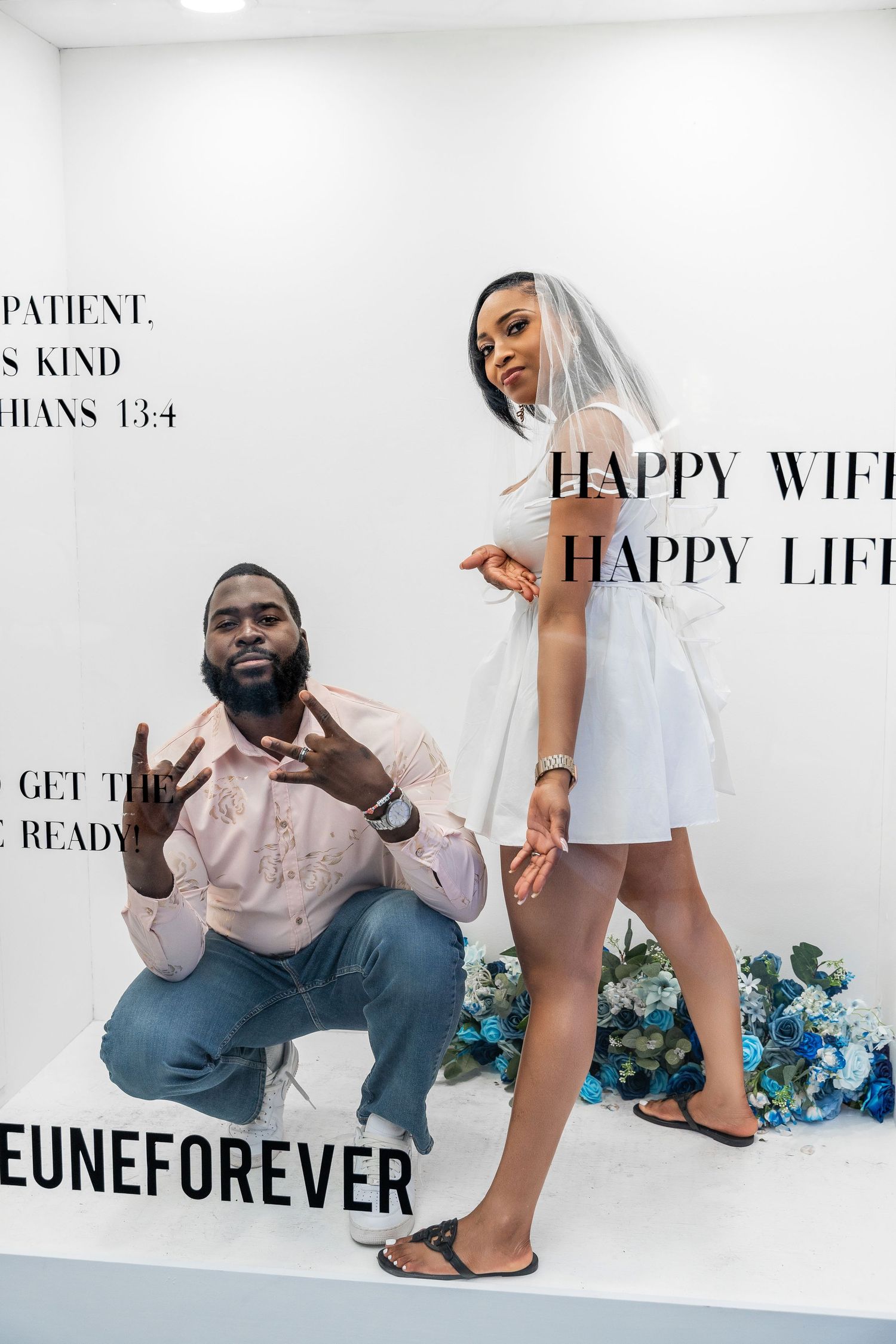 Bride in white dress and veil poses with groom inside The Lejeune's Happy Wife Happy Life photo booth.