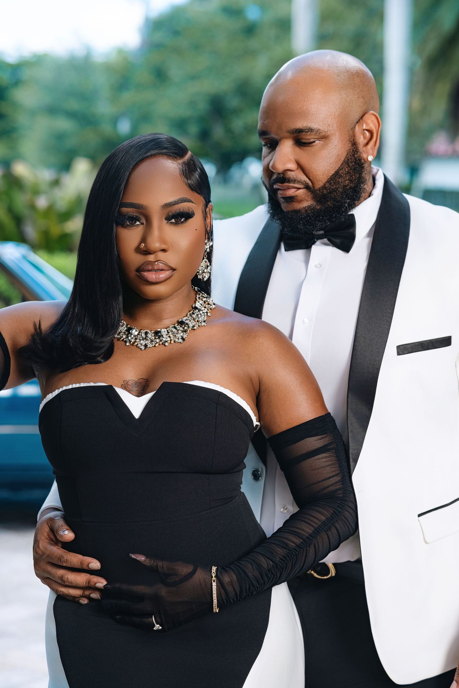 Glamorous Black couple in black strapless gown and white tuxedo pose in sophisticated portrait.